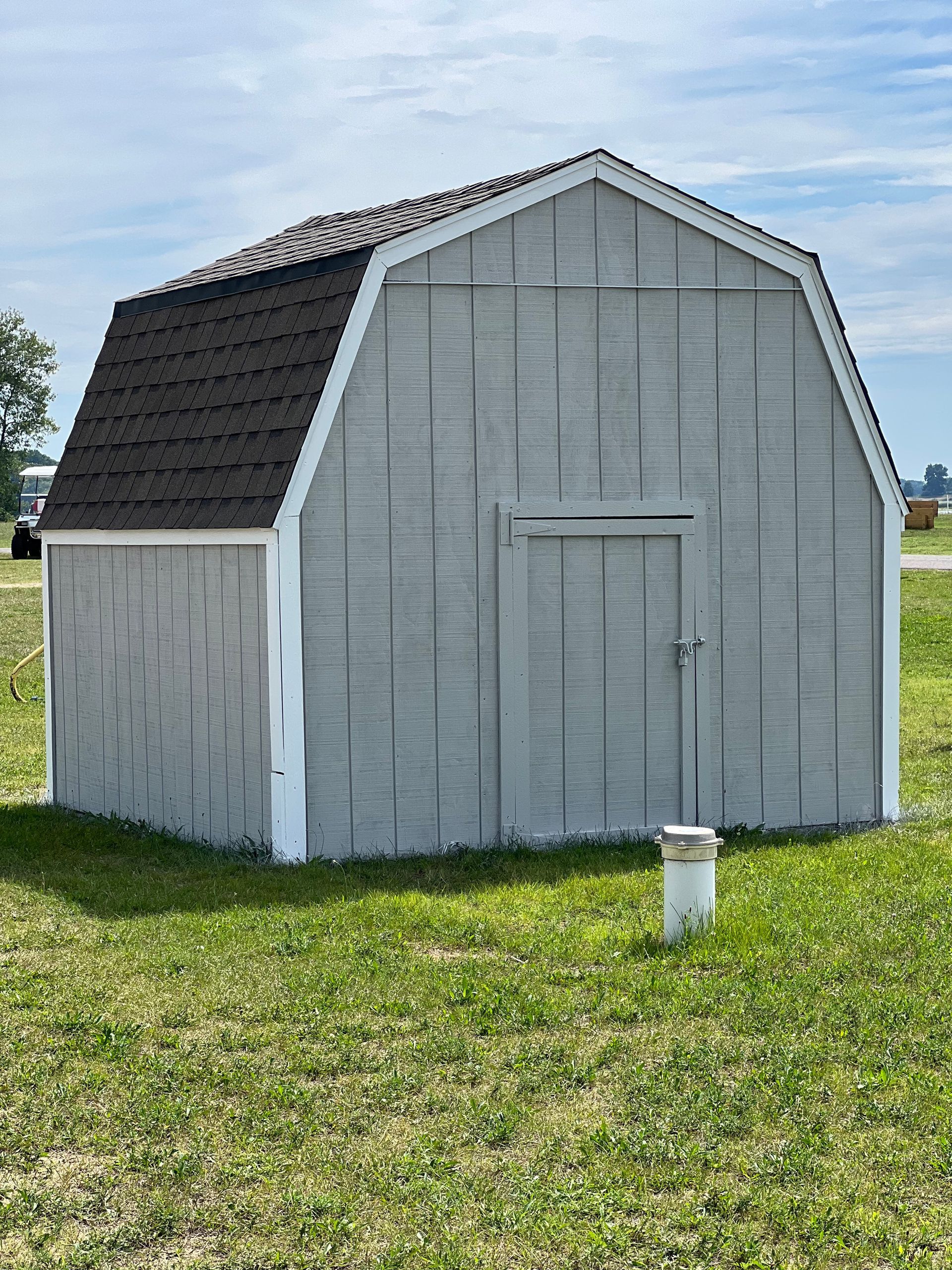 A small barn is sitting in the middle of a grassy field.