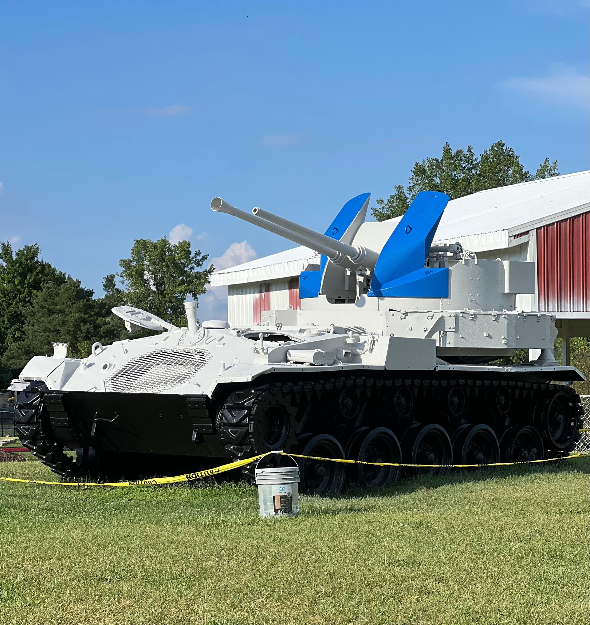A white tank with a blue wing is parked in a grassy field