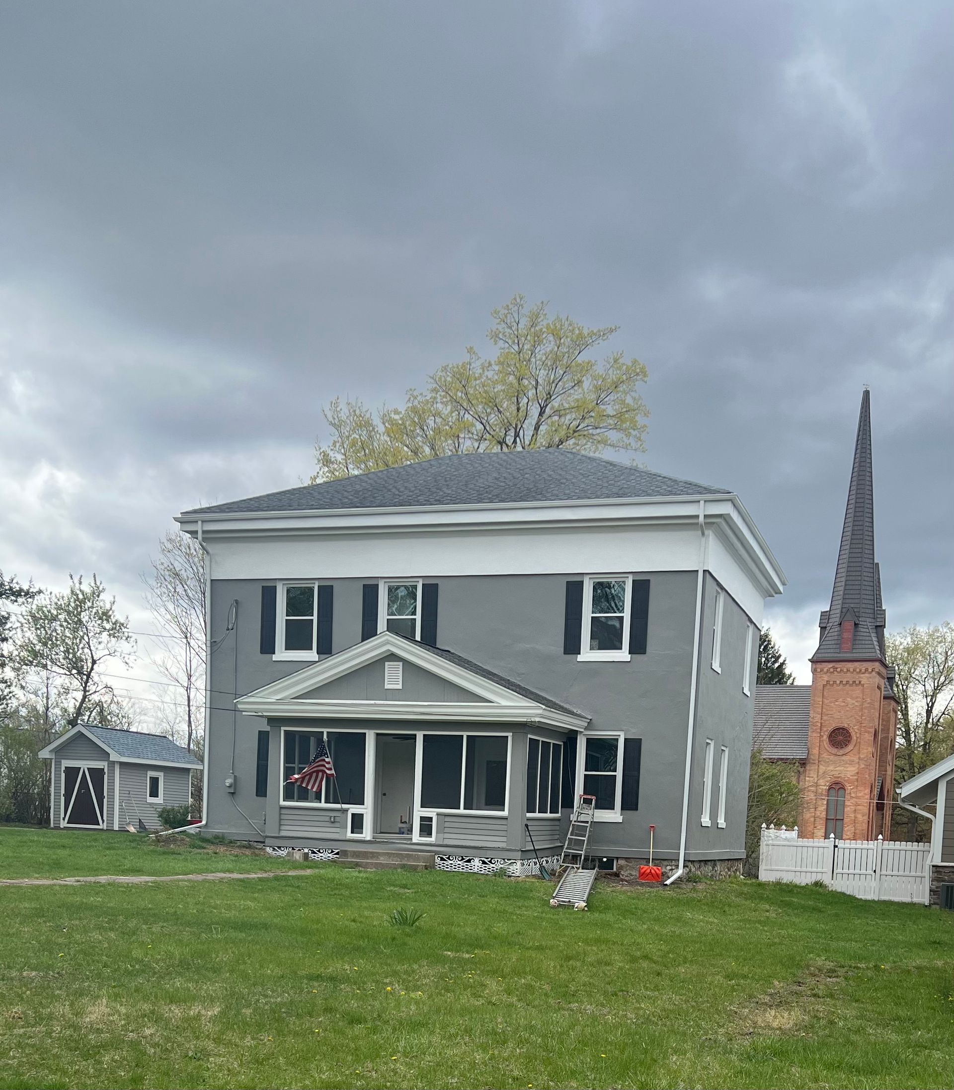A large gray house is sitting in the middle of a lush green field.