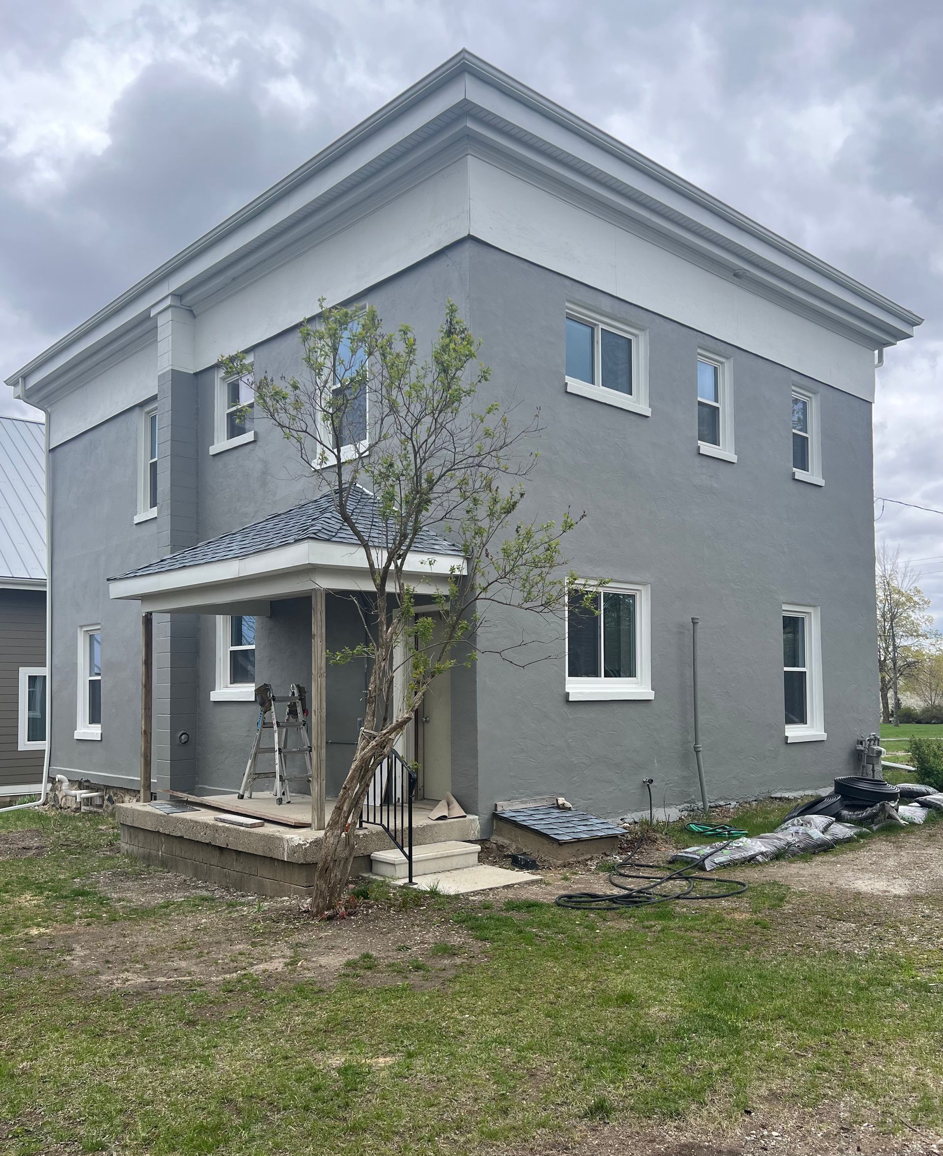 A large gray and white house with a tree in front of it.