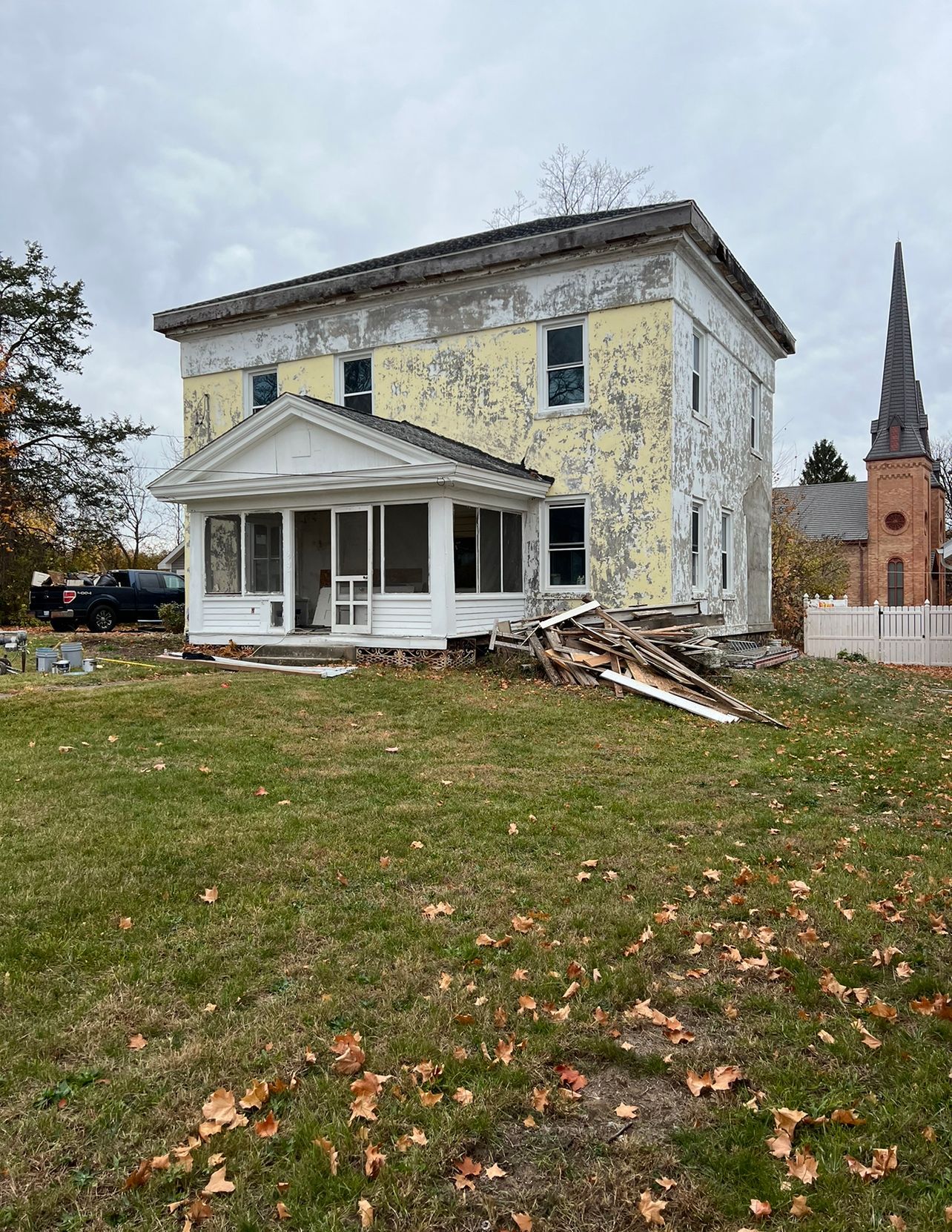 An old house is sitting in the middle of a grassy field next to a church.