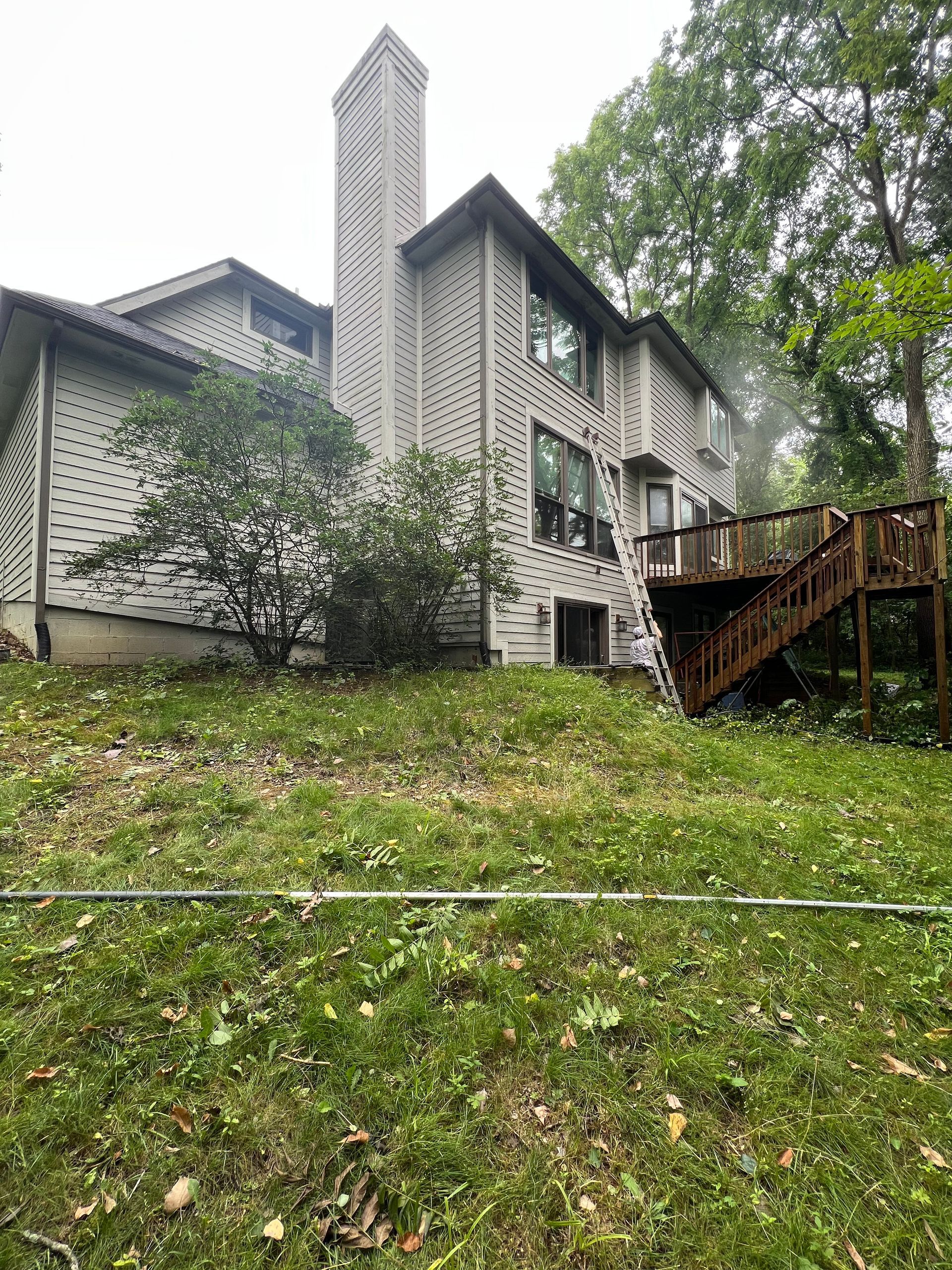 A large house with a deck and stairs is sitting on top of a grassy hill.