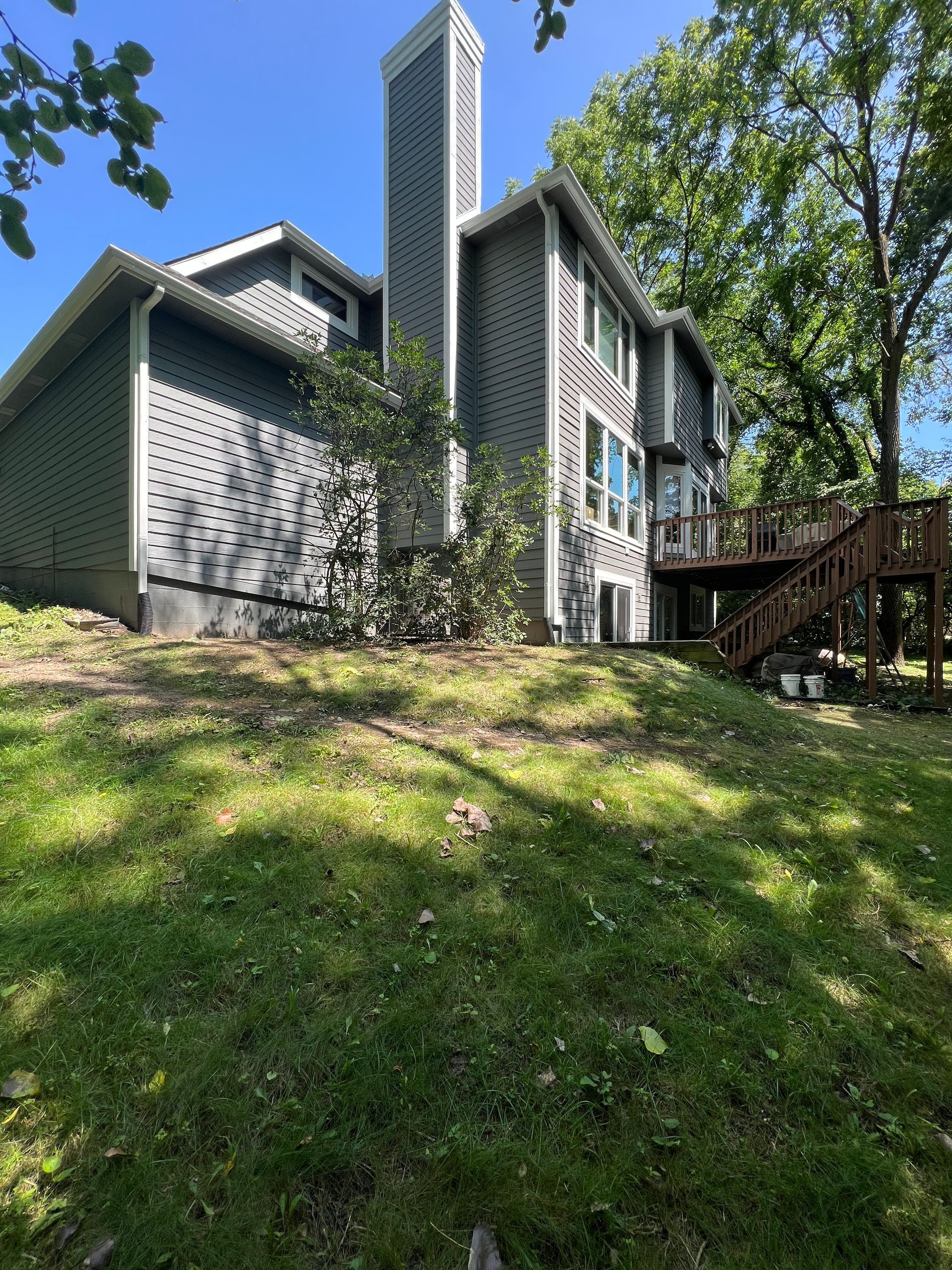 A large house with a large deck is sitting on top of a grassy hill.