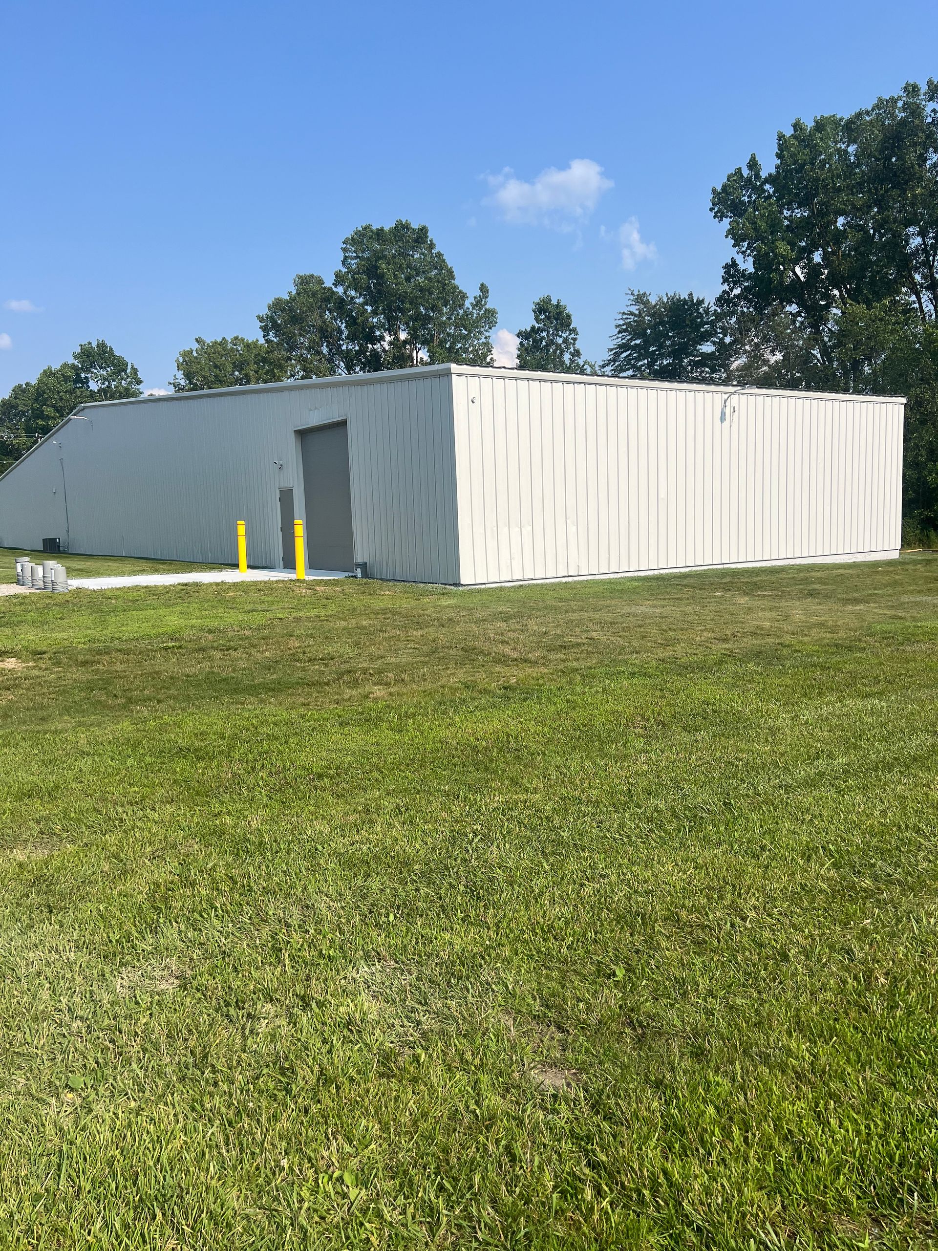 A large white building is sitting in the middle of a grassy field.
