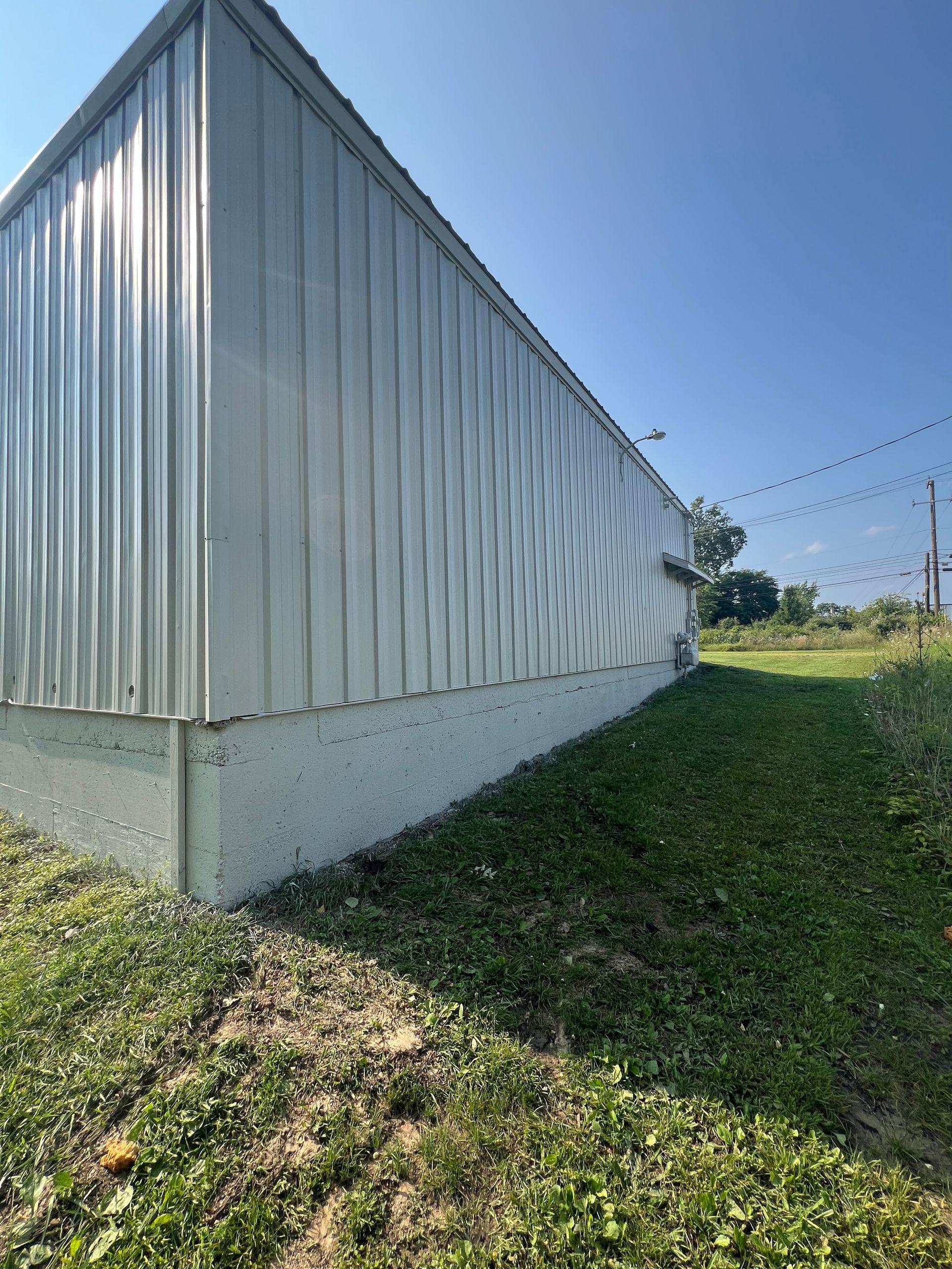 A white metal building is sitting in the middle of a grassy field.