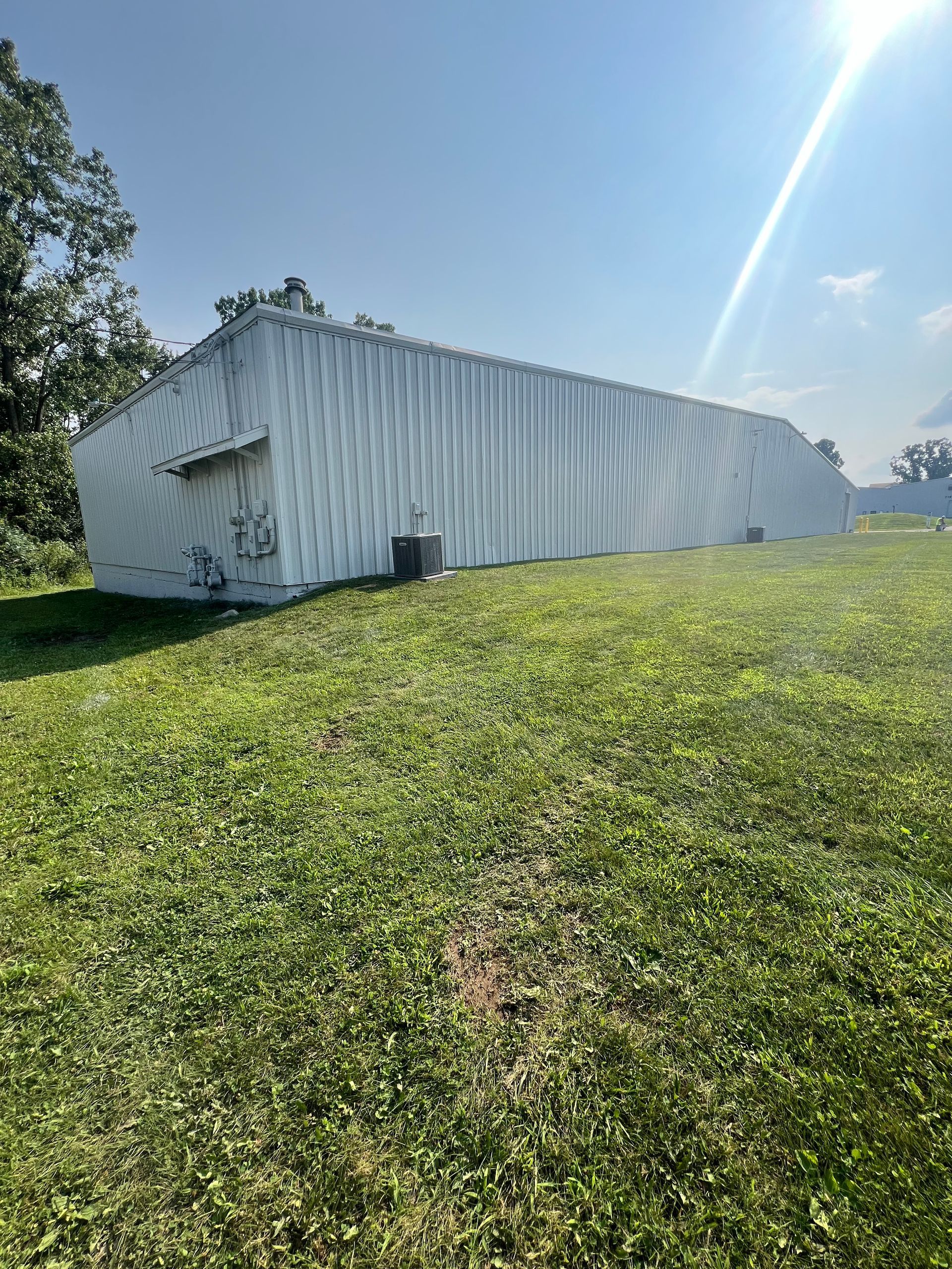 A large white building is sitting in the middle of a grassy field.