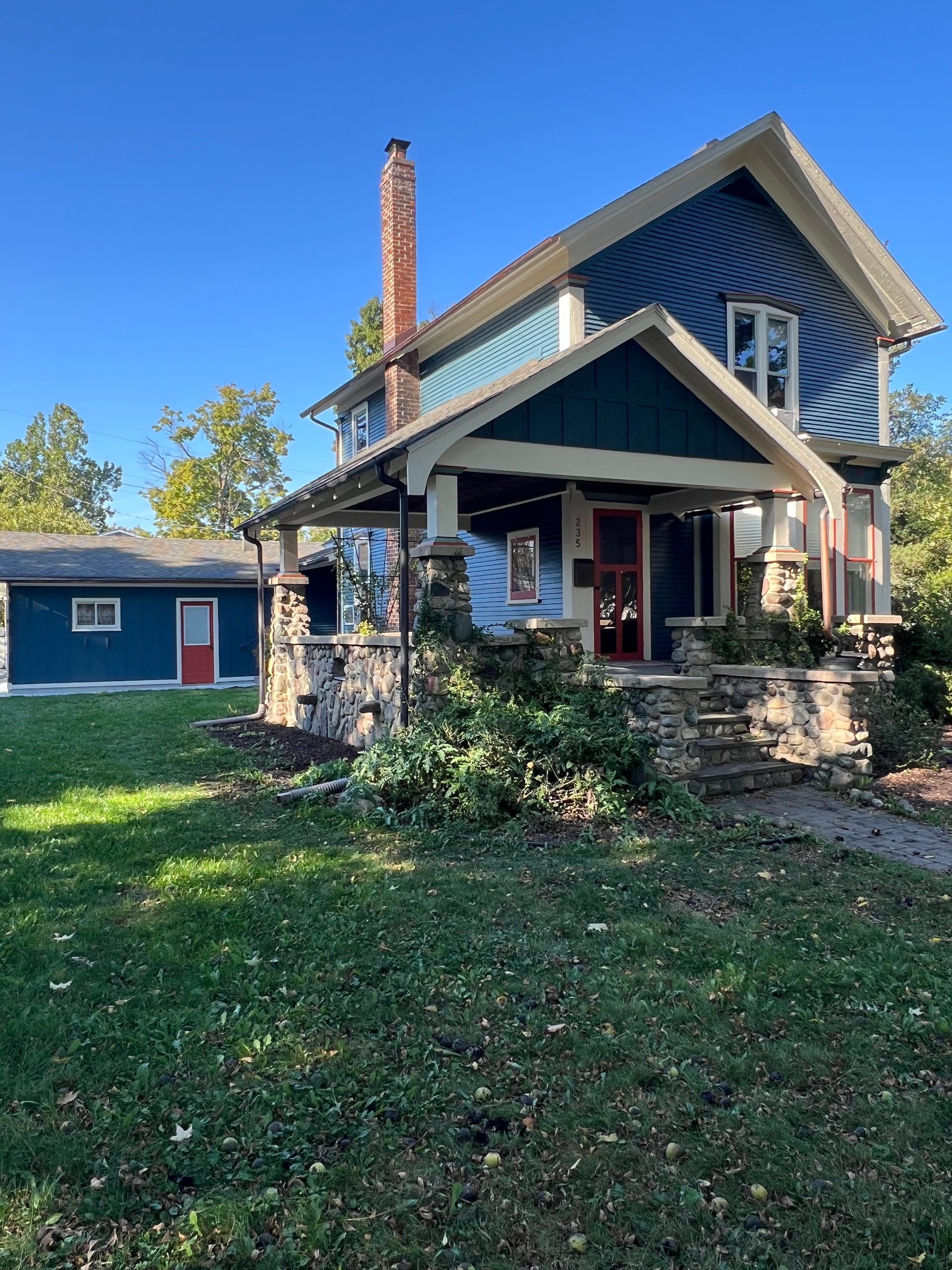 A blue house with a red door and a chimney is sitting on top of a lush green lawn.