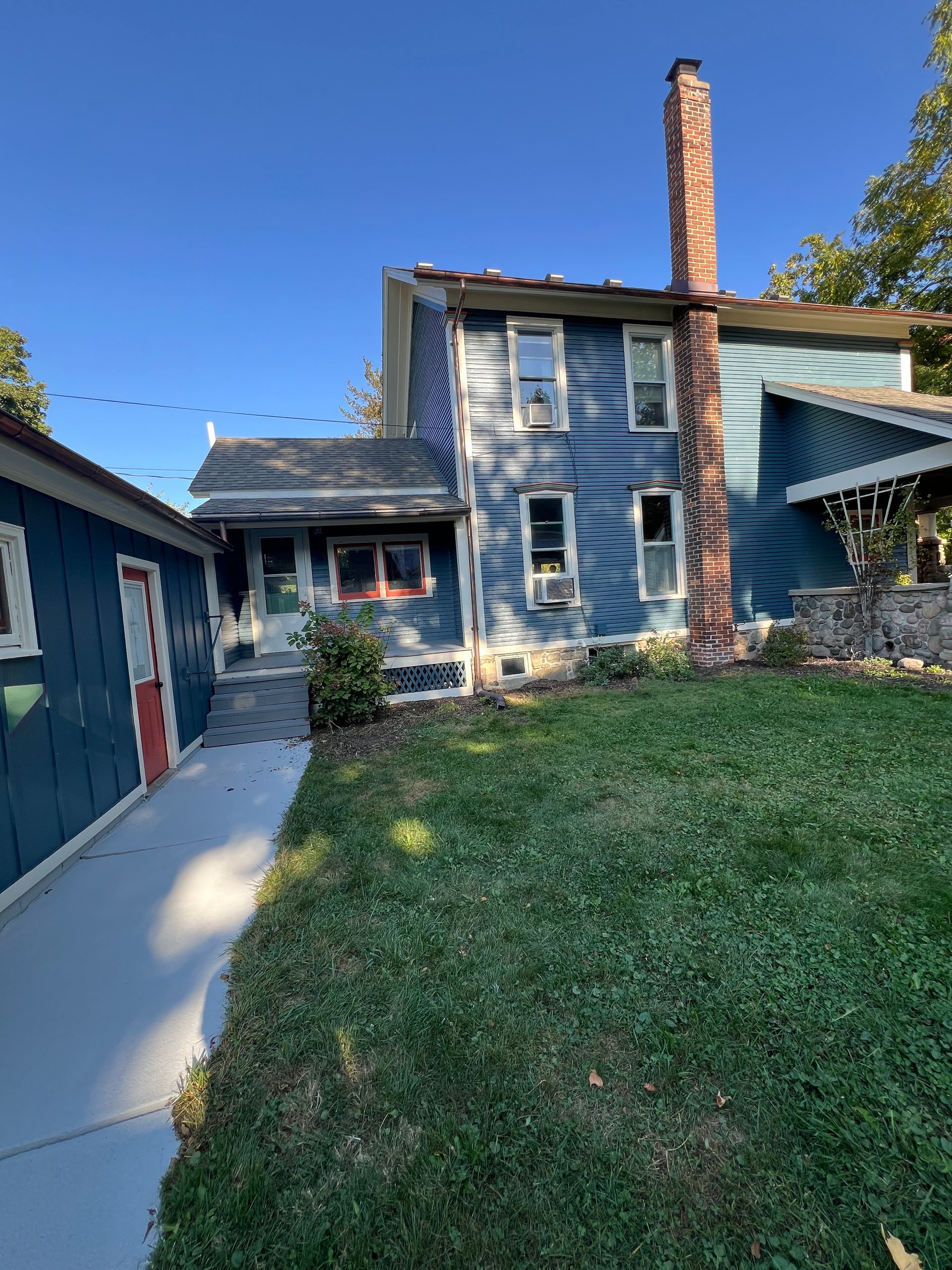 A blue house with a brick chimney is sitting on top of a lush green lawn.