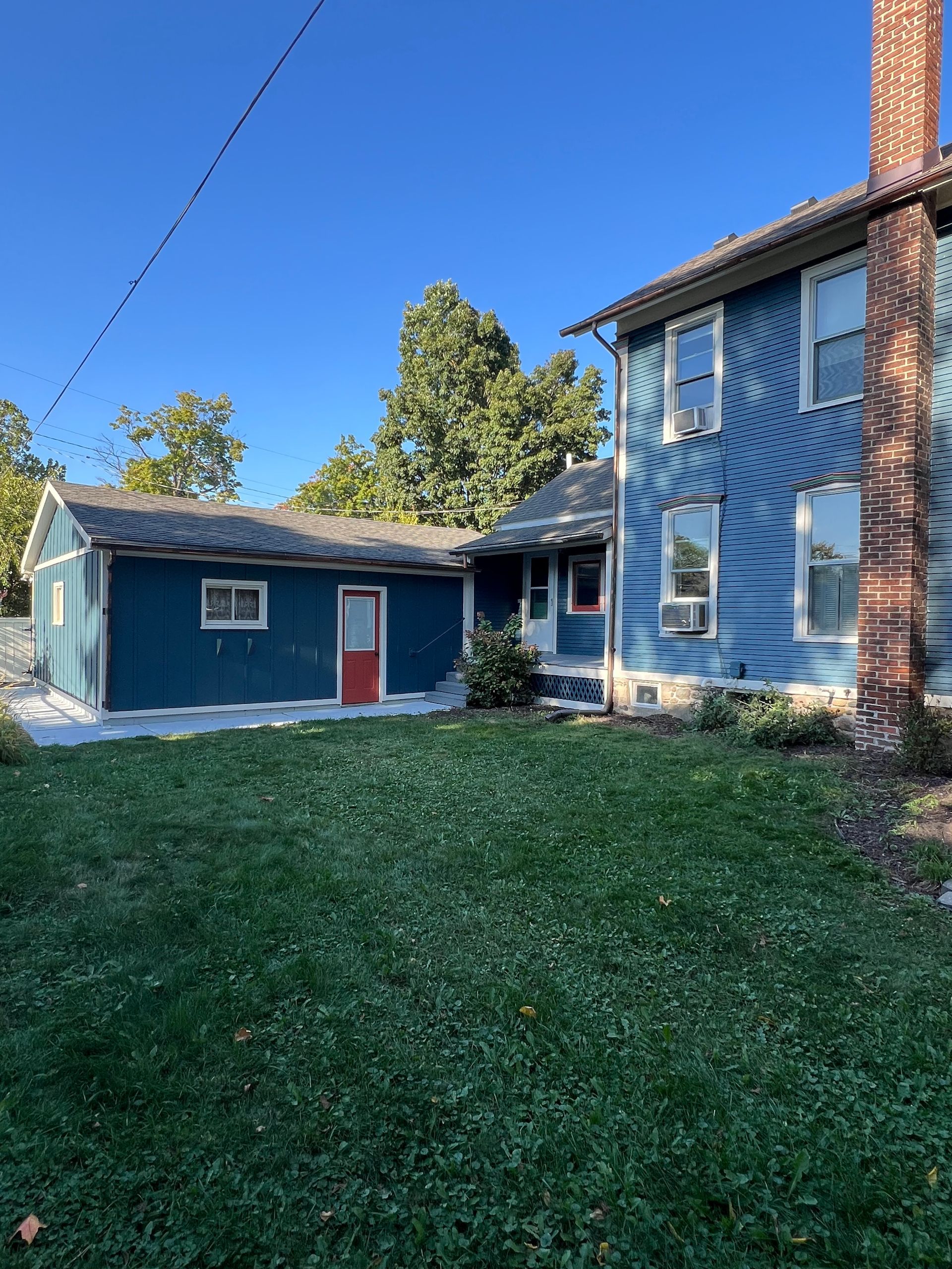 A blue house with a red door is sitting on top of a lush green lawn.
