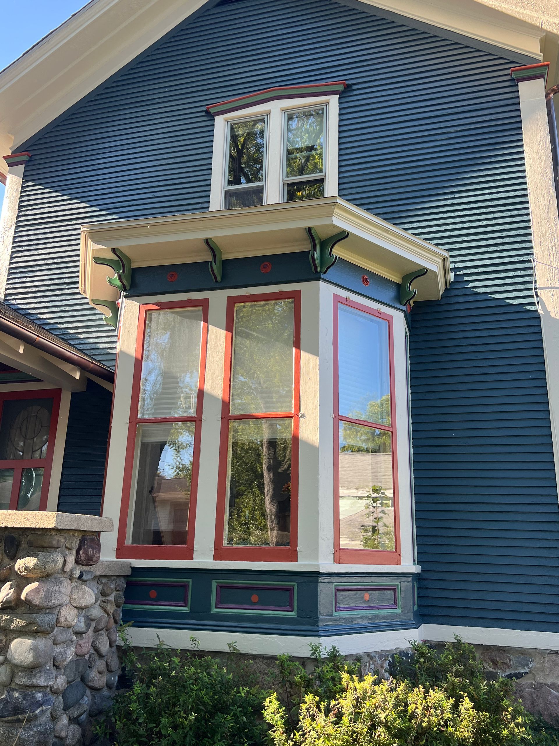 A blue house with a red and white bay window