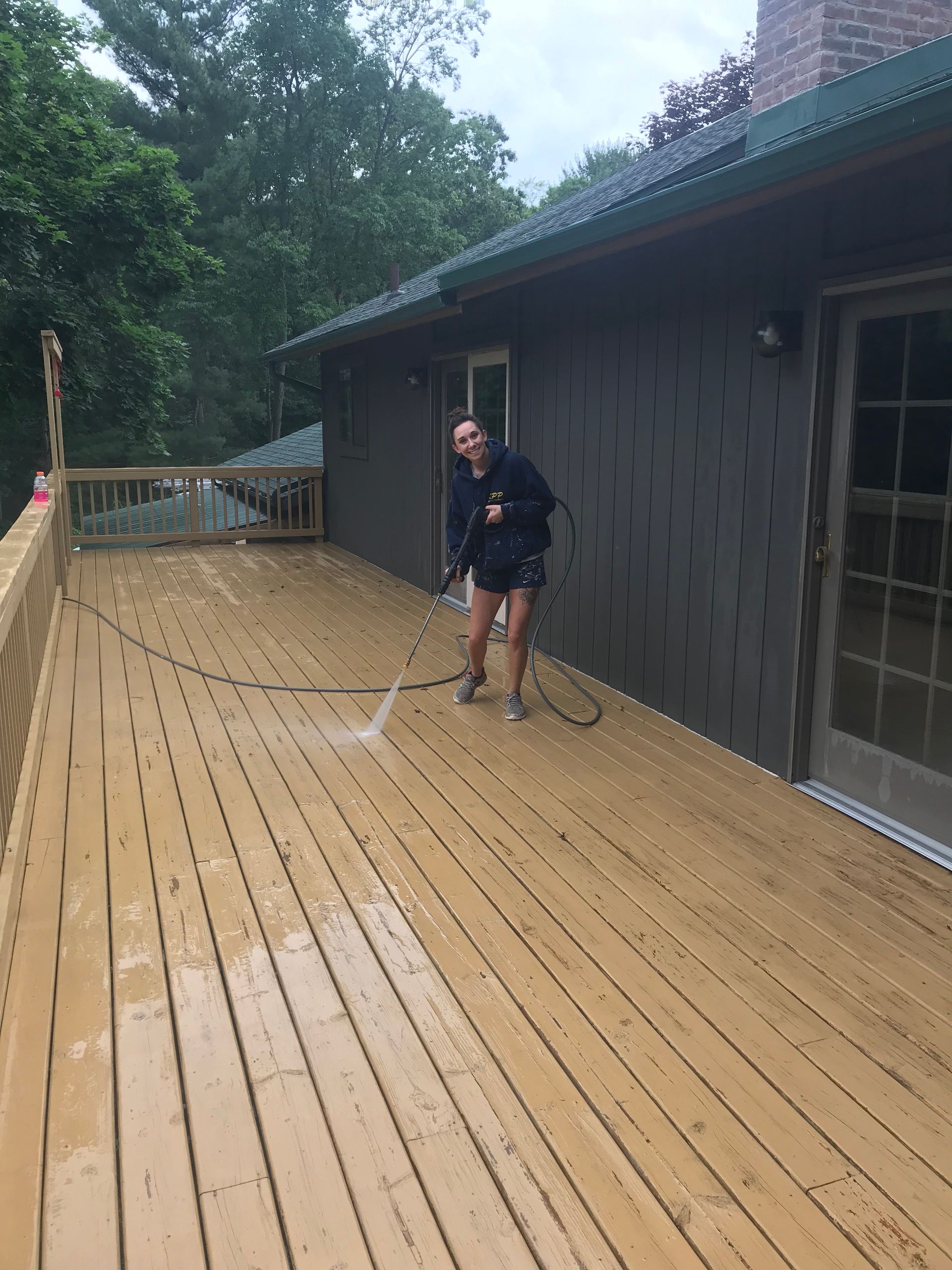 A woman is cleaning a wooden deck with a pressure washer.