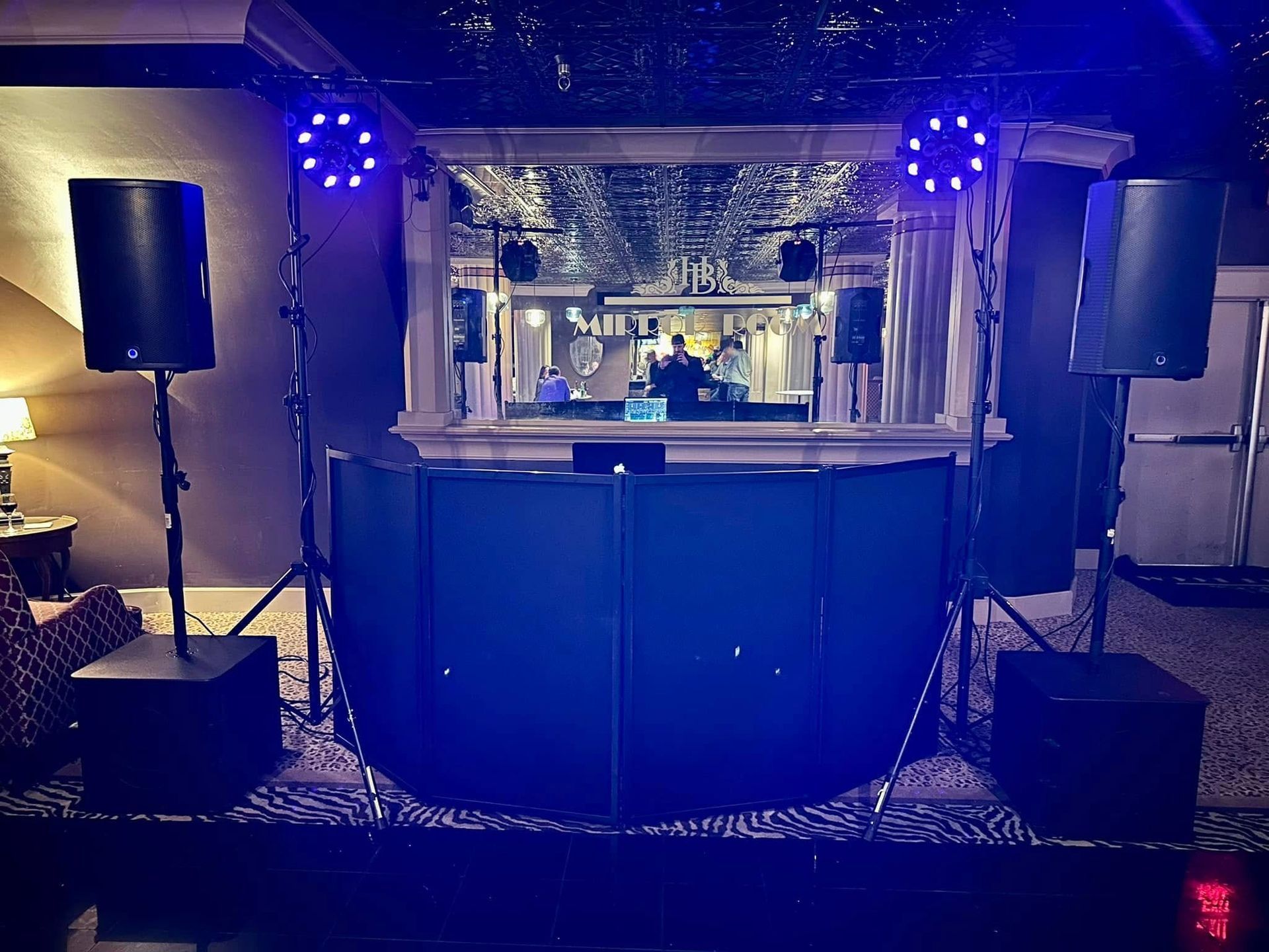 A DJ setup with speakers, lighting, and a front screen in a dark room with blue ambient lighting.
