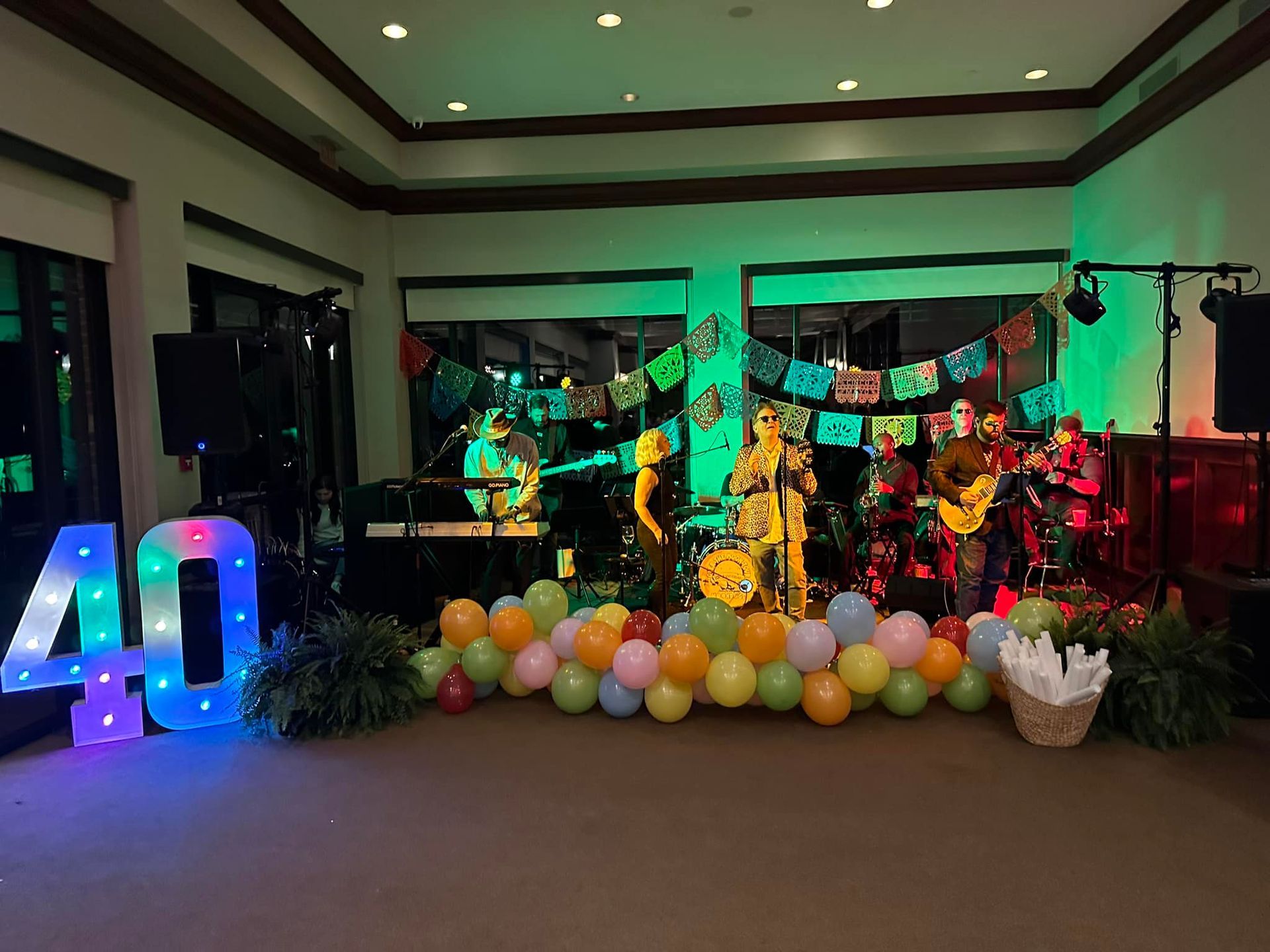 A live band plays on a stage decorated with colorful bunting, with light-up 