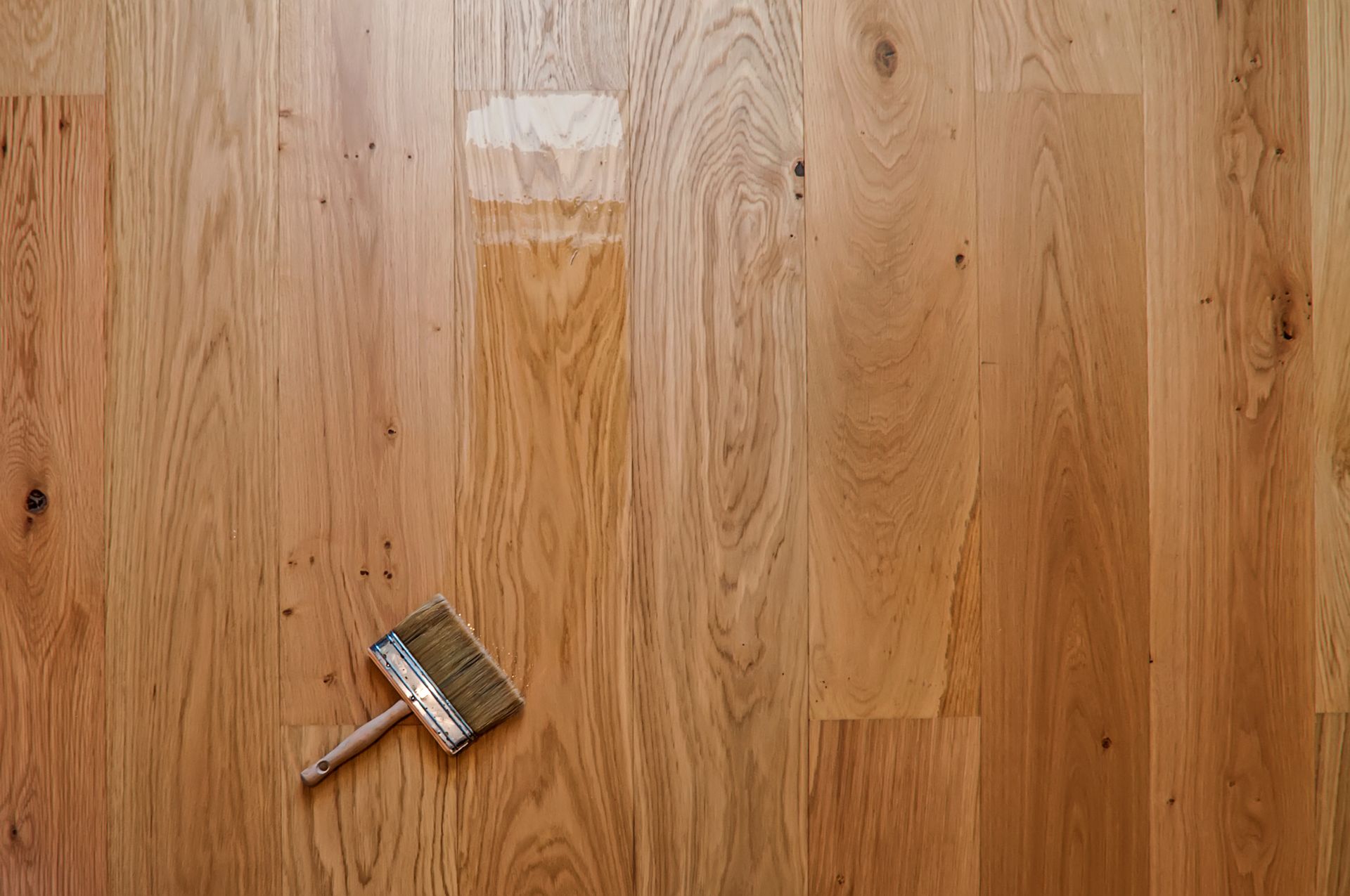 Wooden floor being stained, with a paintbrush lying on the surface