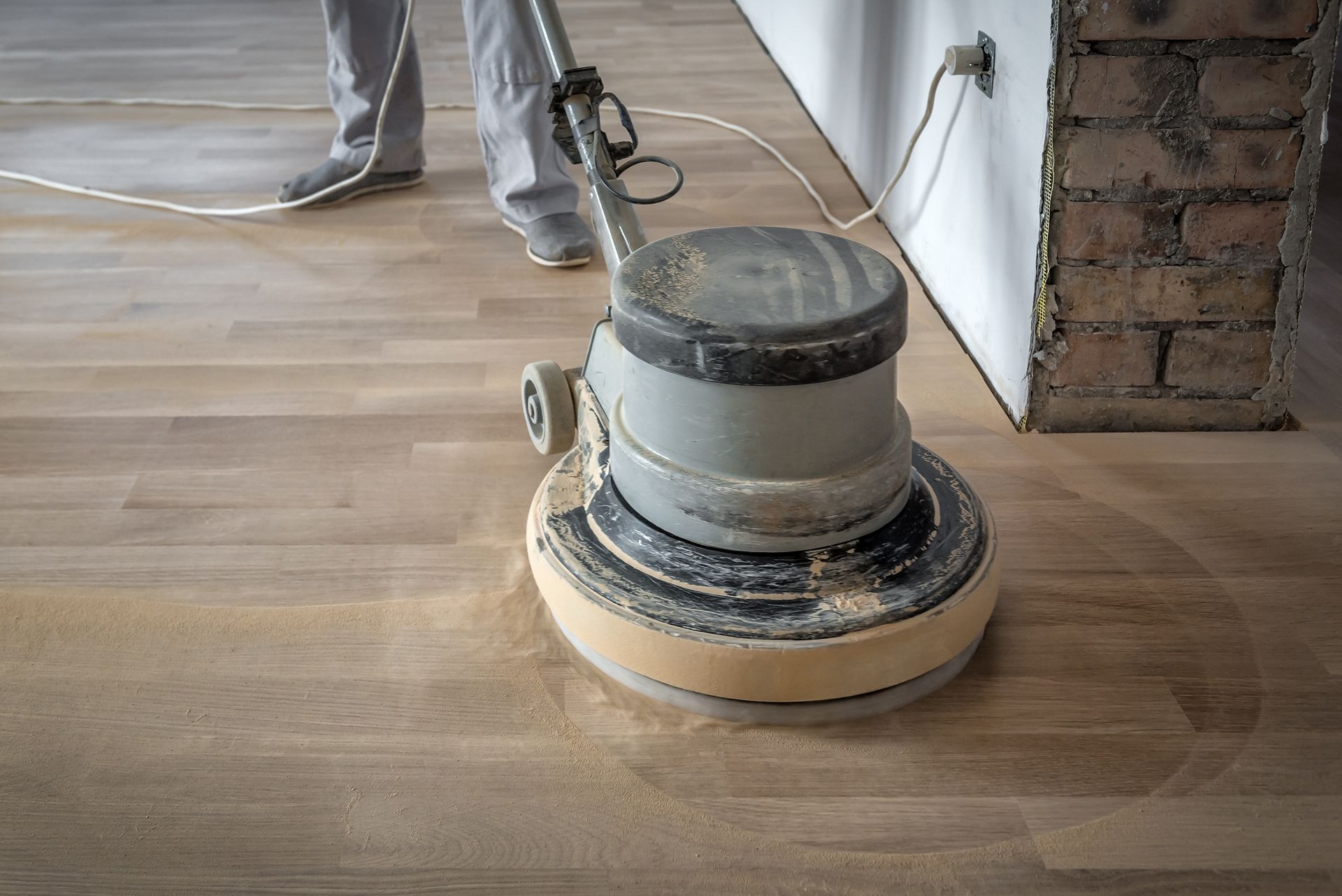 Person sanding a wooden floor with a floor polisher