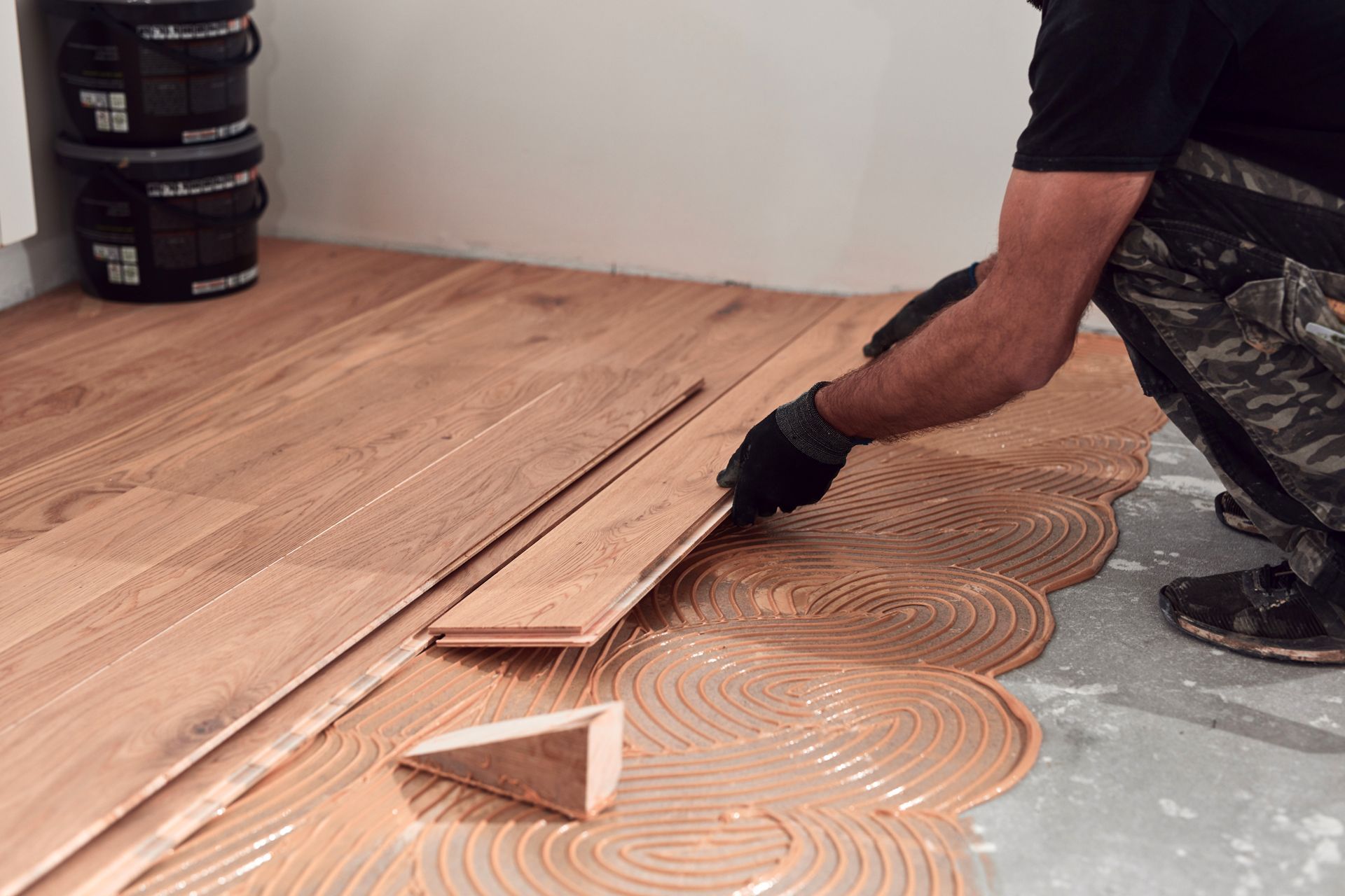 Person installing wooden floorboards, applying glue to the concrete subfloor in a room