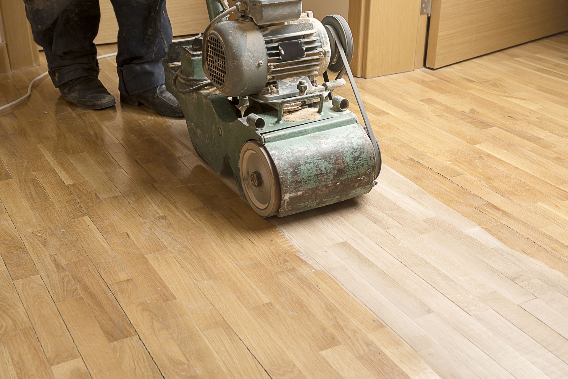 Person sanding a hardwood floor with a large machine, revealing a lighter wood color