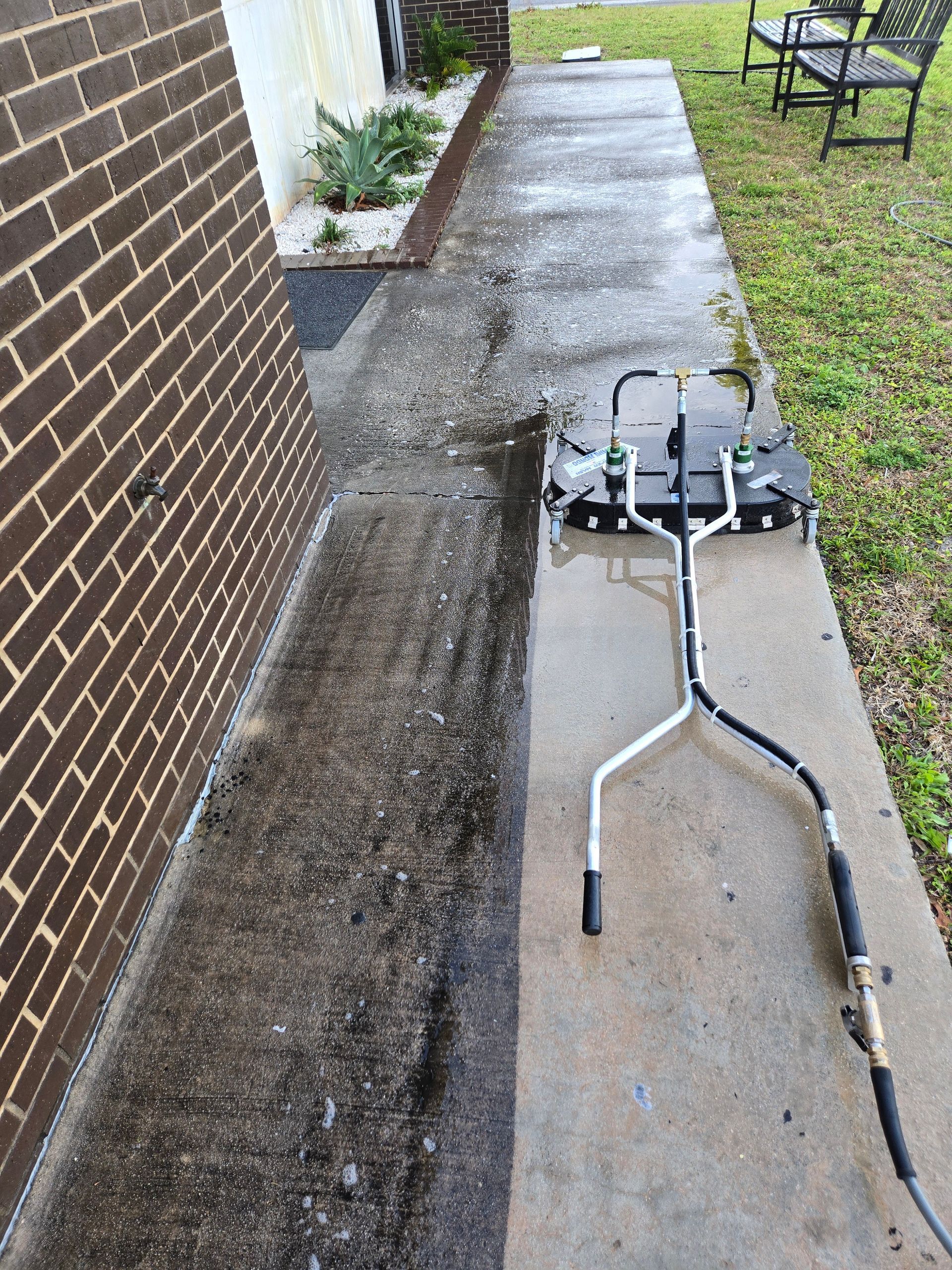 A person pressure washing a concrete walkway next to a brick building.