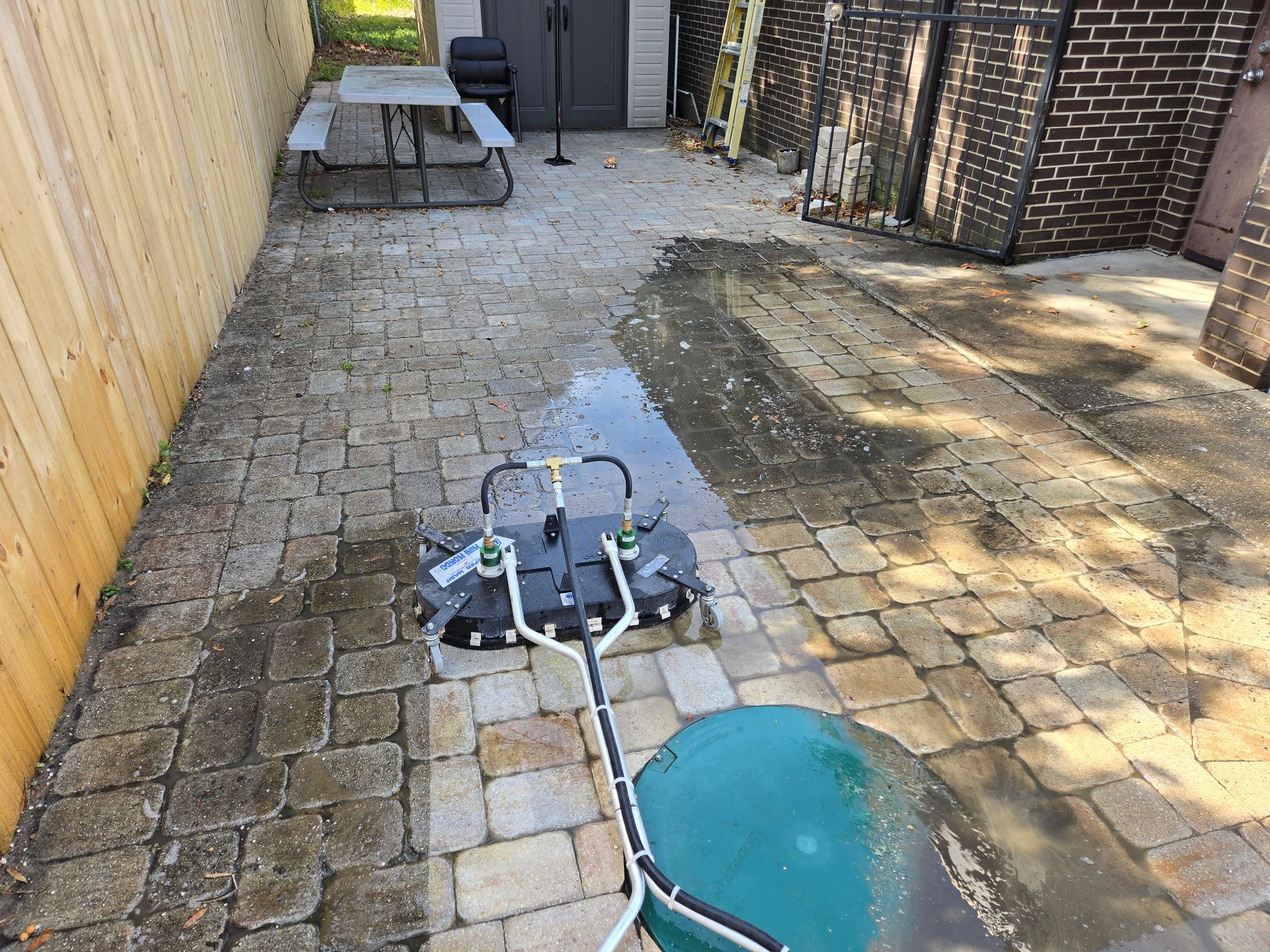 A person power washing a brick patio; water sprays from the cleaner.