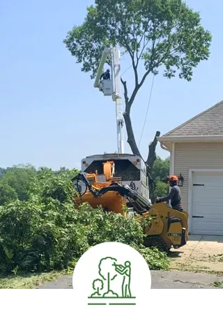 A man is cutting a tree with a machine in front of a house.