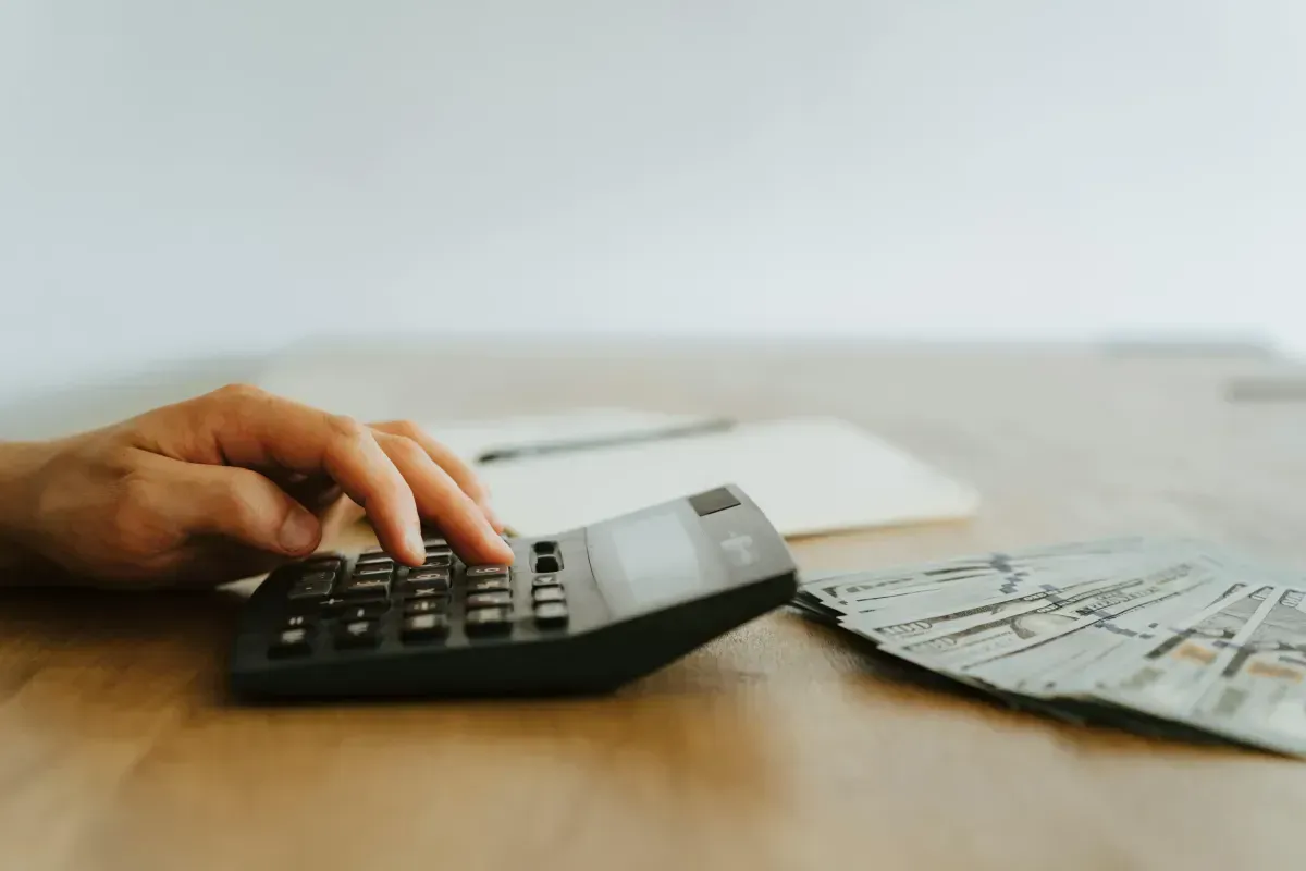 A person is using a calculator on a wooden table.