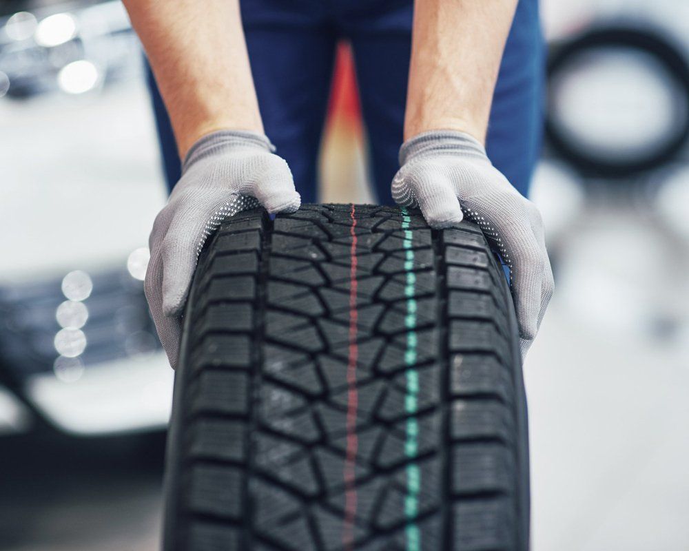 A Man Wearing Gloves is Holding a Tire — Coolangatta Automotive in Coolangatta, QLD