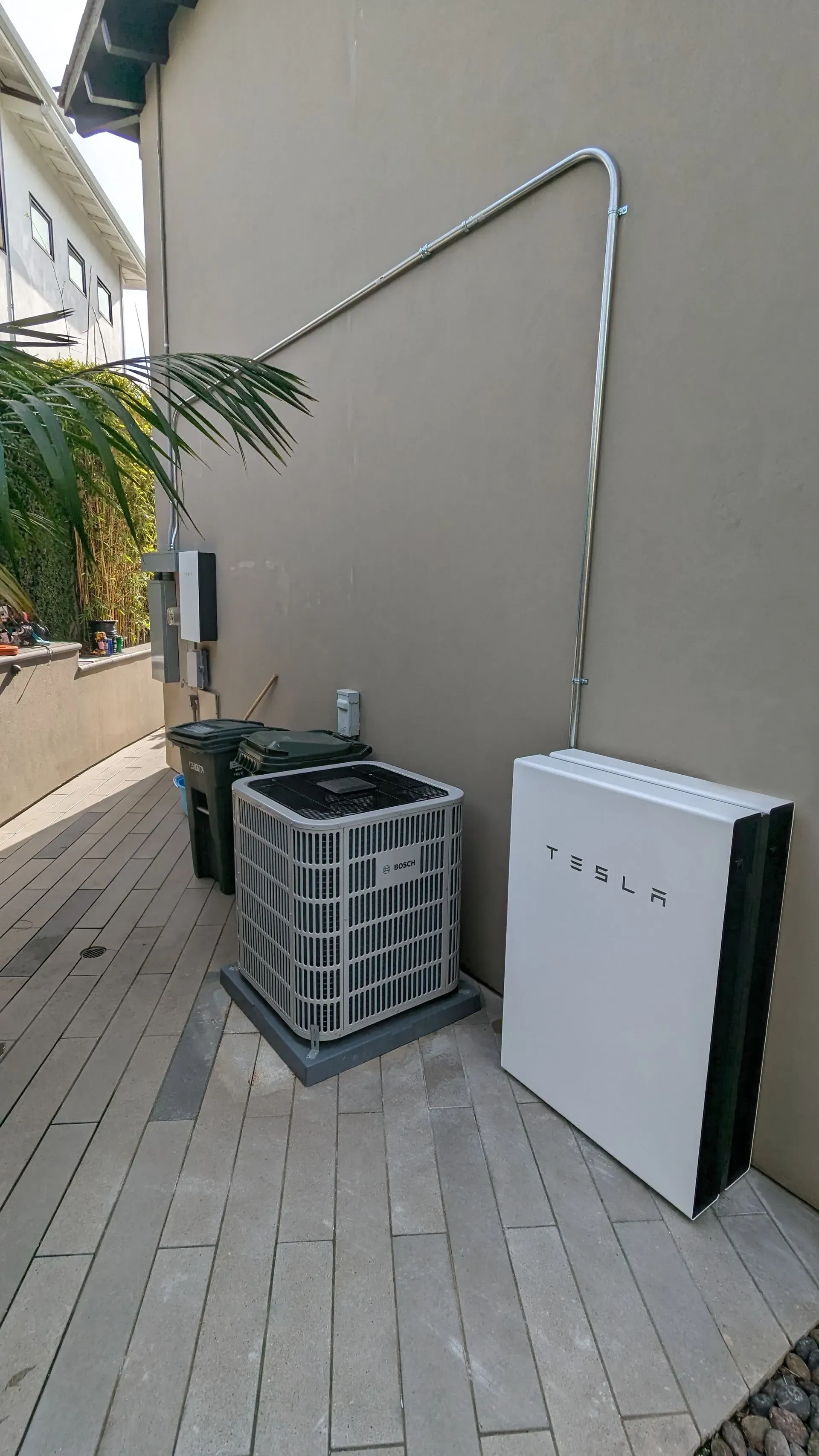 A tesla solar panel is sitting on the side of a building next to an air conditioner.