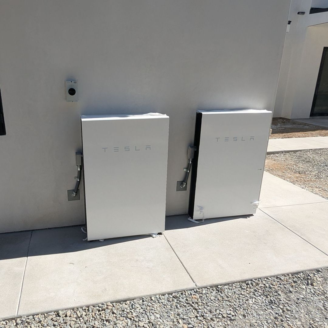 Two white tesla batteries are sitting on a sidewalk next to a building.