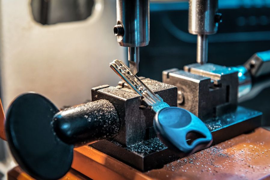 Key being cut by machine; metal shavings visible. Blue-handled key in progress.