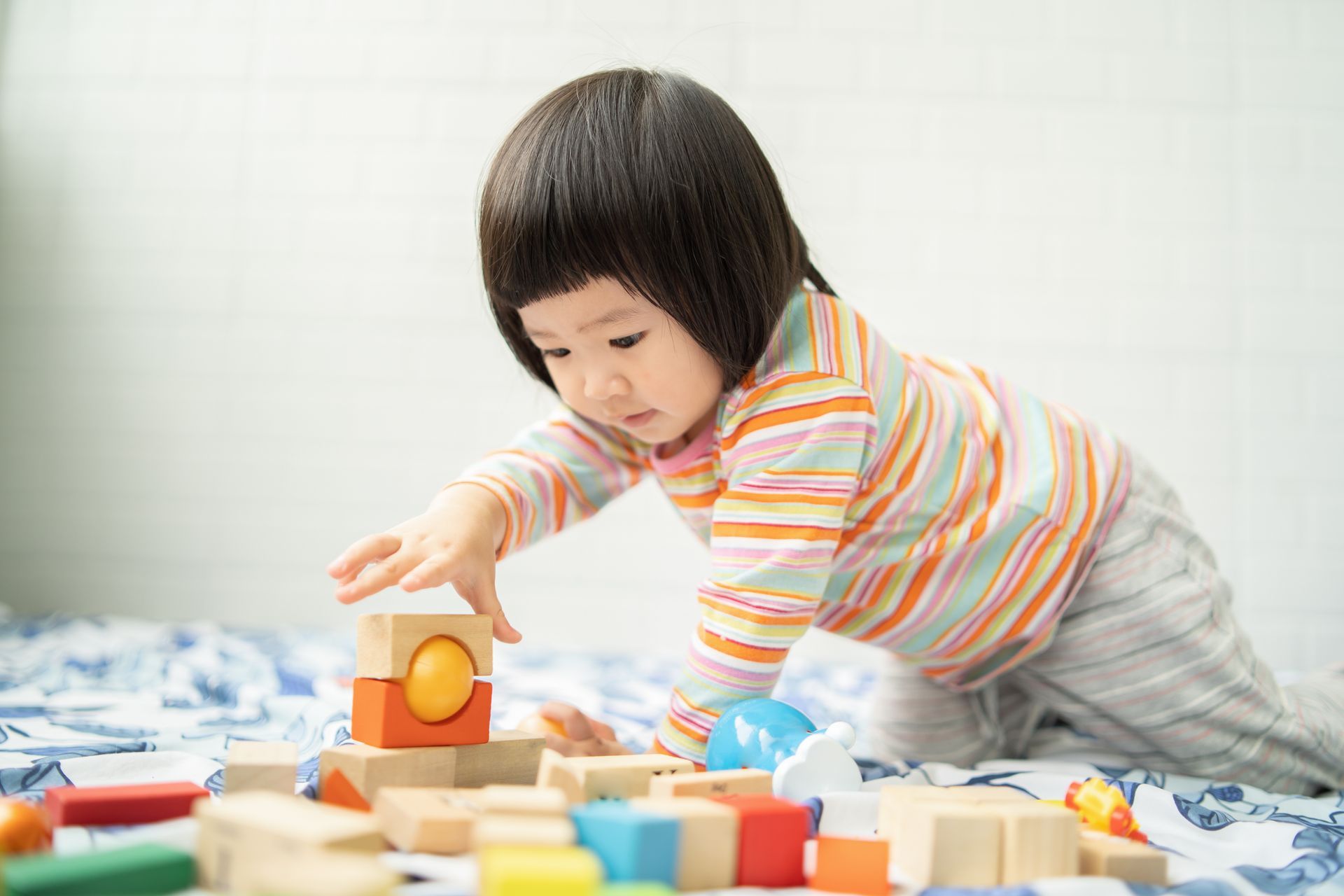 A little girl is playing with wooden blocks on a bed.