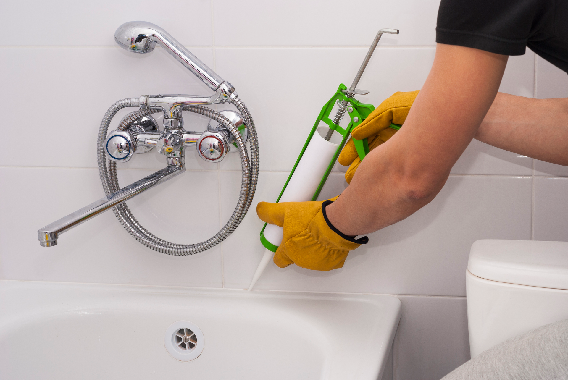 A person is applying caulk to a bathtub in a bathroom.