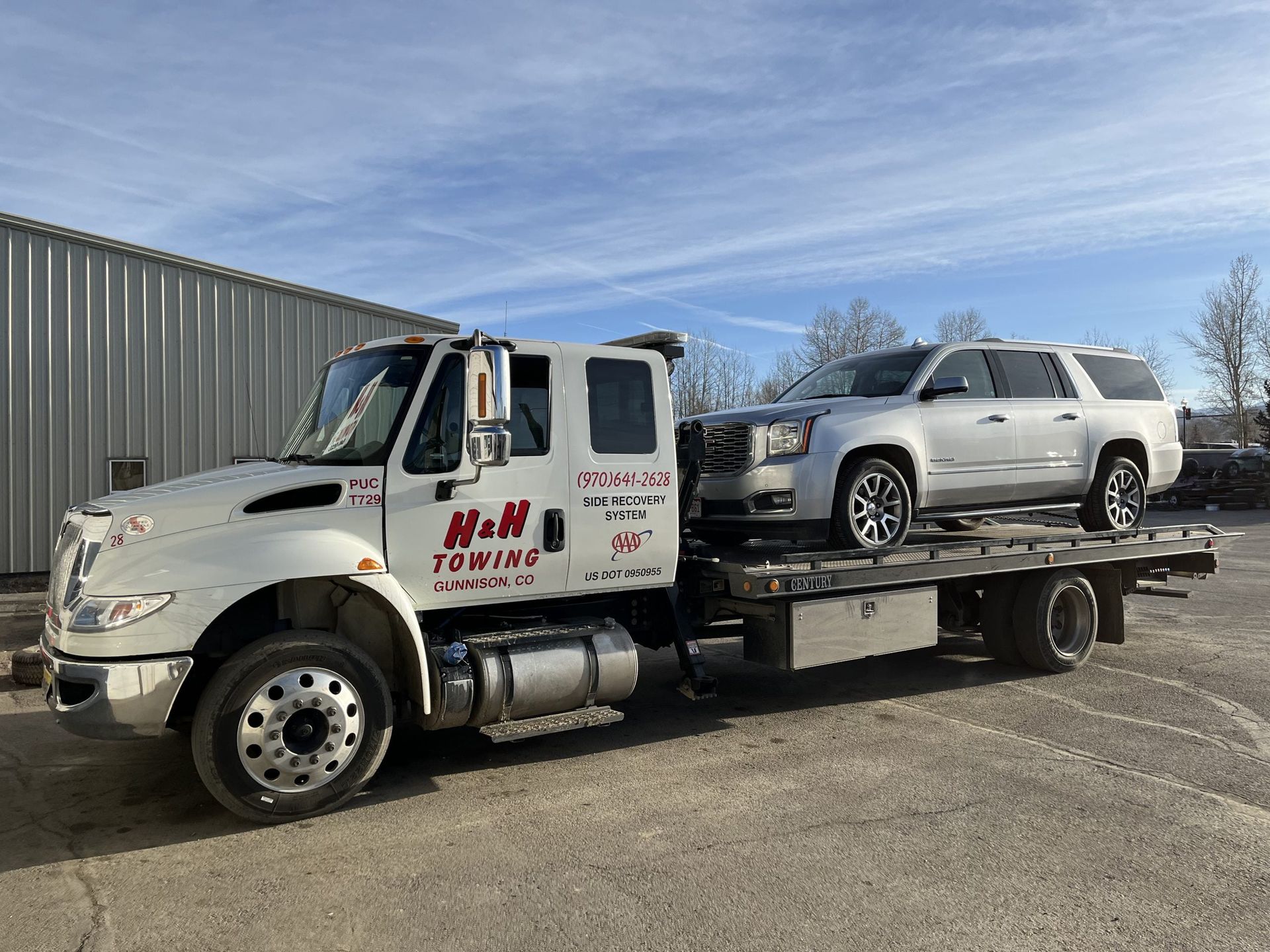Tow truck with a silver SUV on the flatbed, parked outside. 
