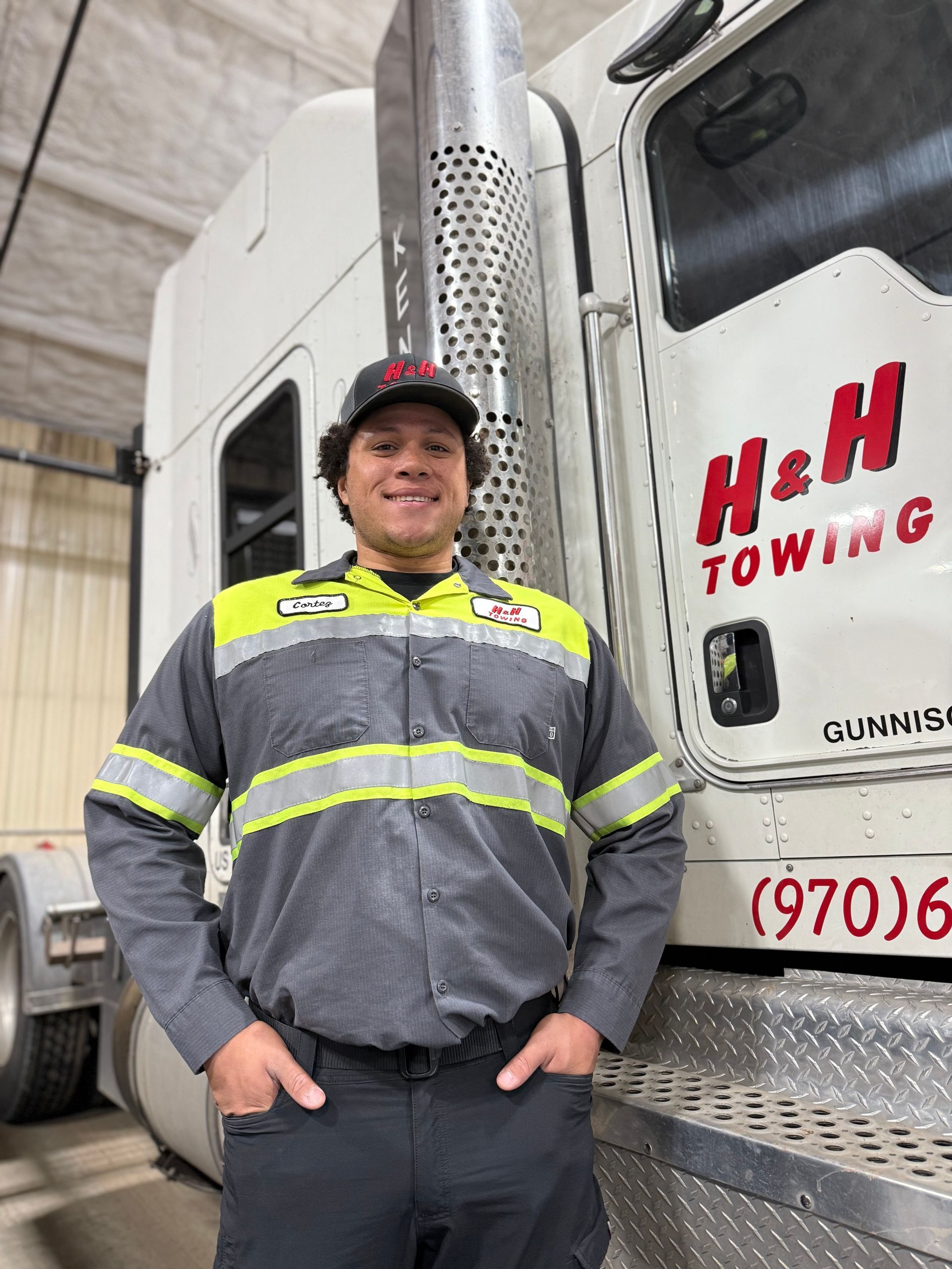 Smiling person in a uniform, standing next to a tow truck with 