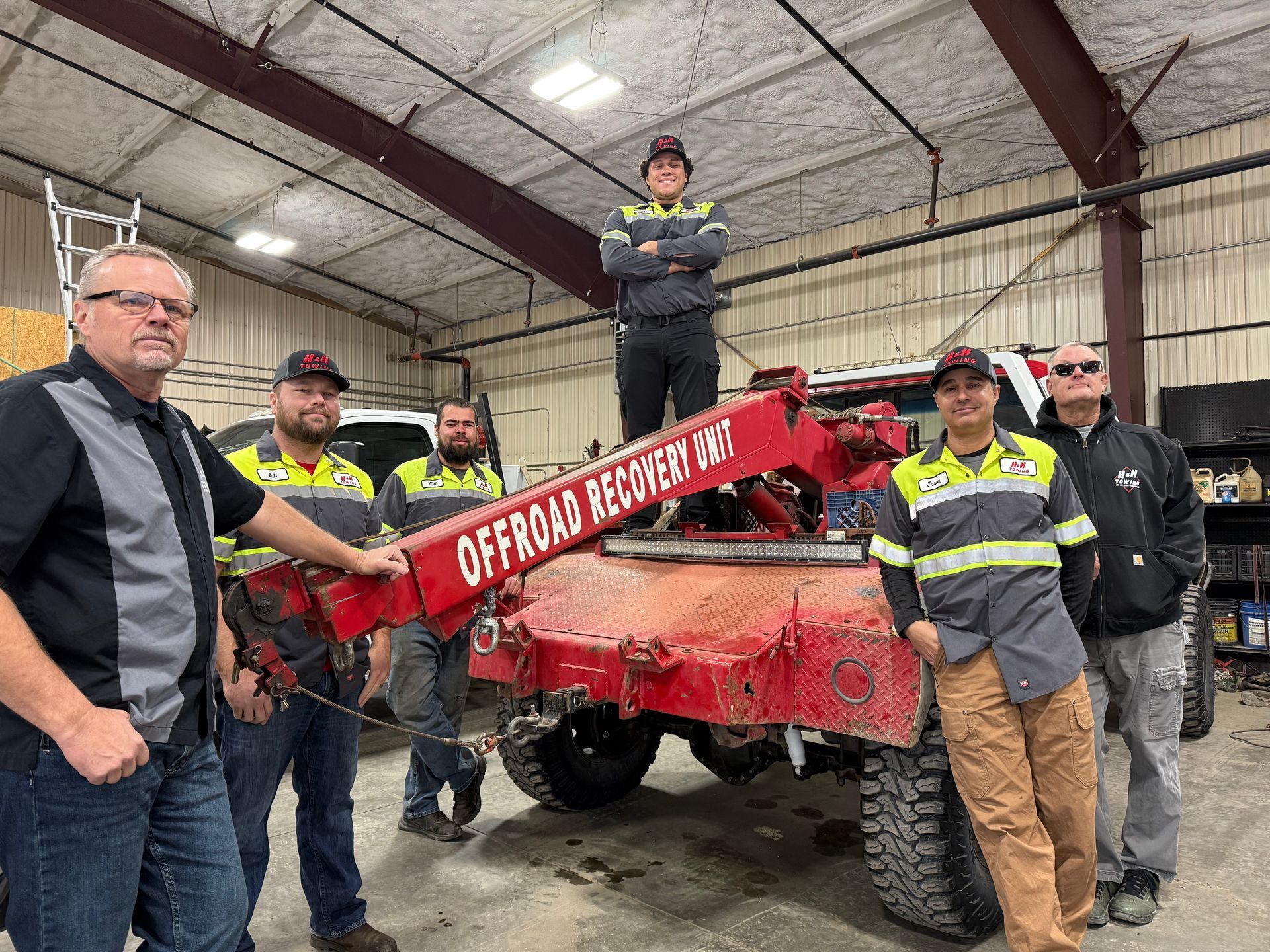Group of tow truck operators posing with a red tow truck in a garage.