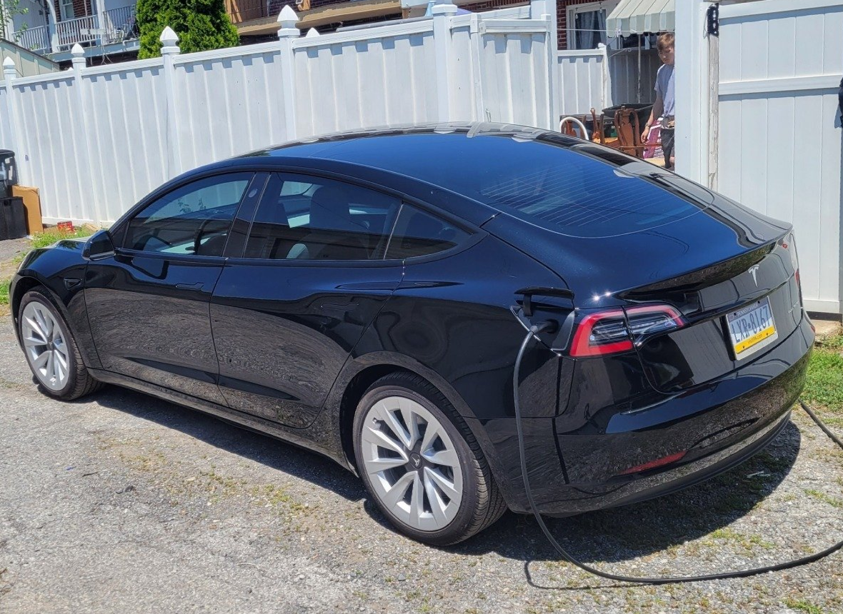 a black tesla model 3 is plugged into a charging station .