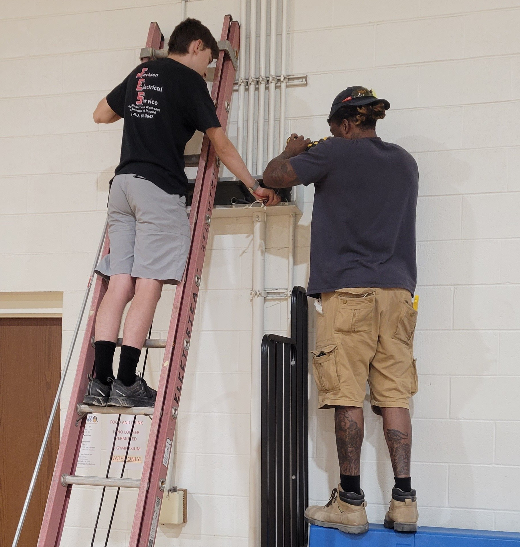 a man on a ladder works with another man with electrical works