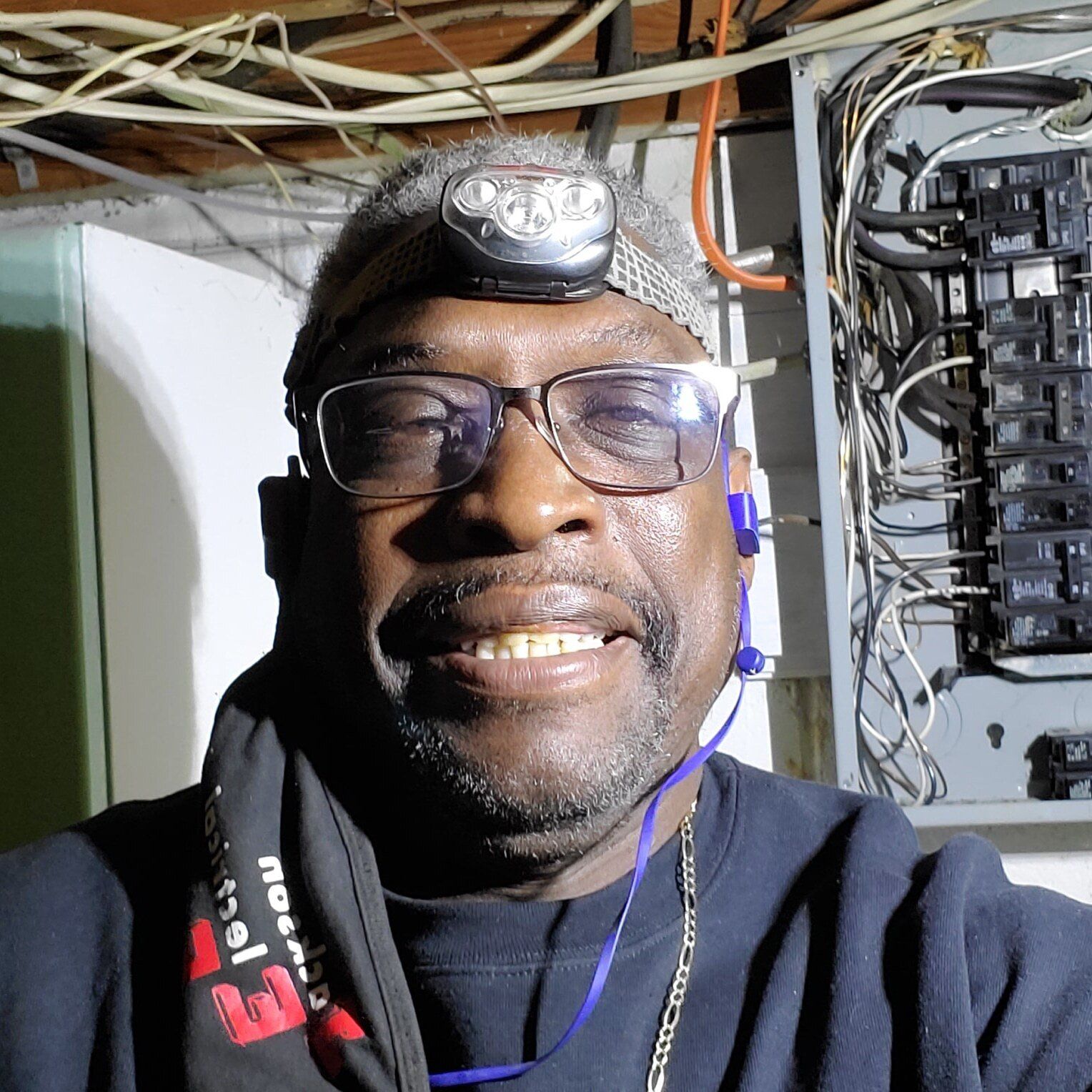 a man wearing glasses and a headlamp is smiling in front of a electrical box .