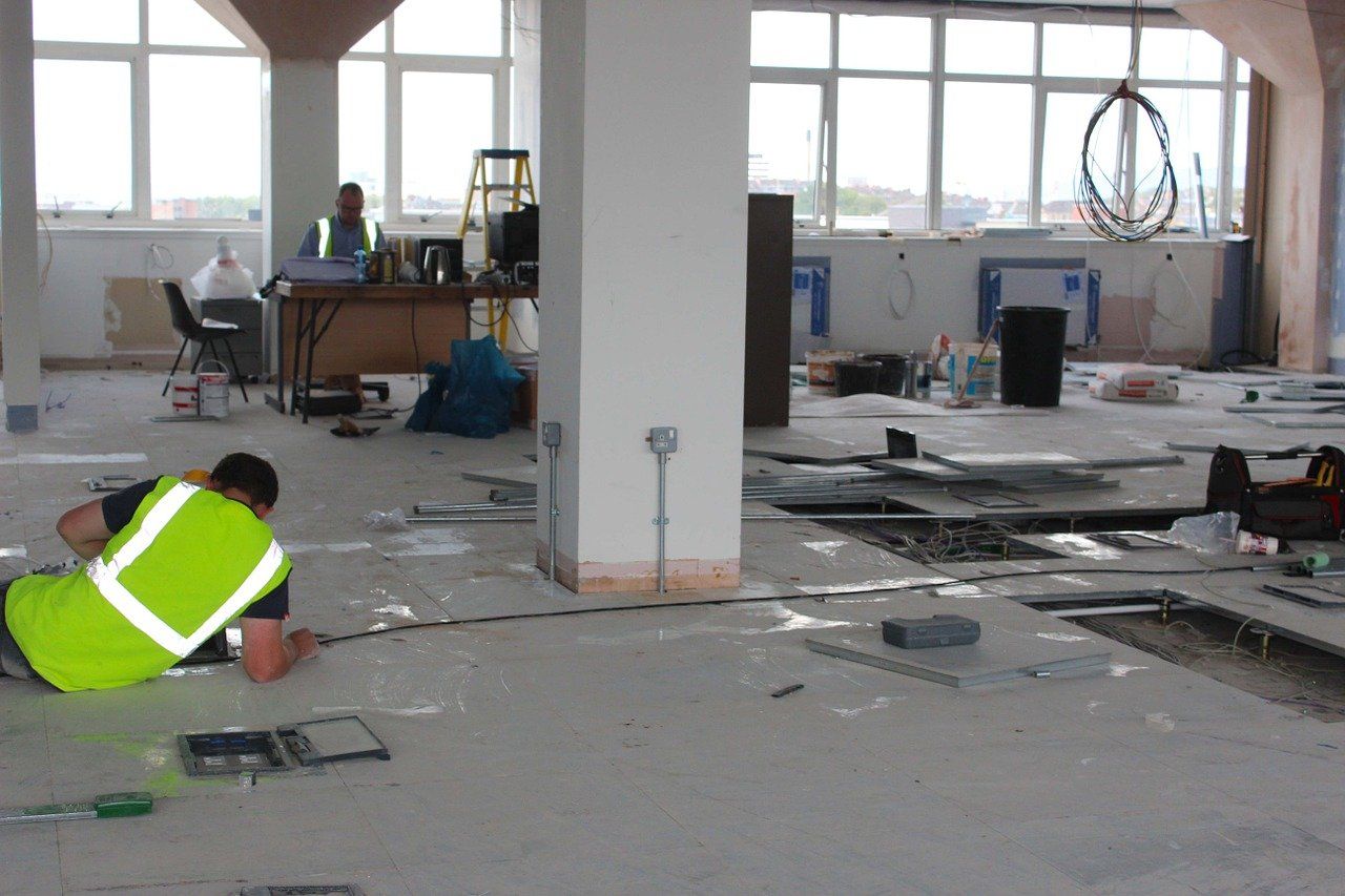 a man in a green vest is working on the floor of a building .