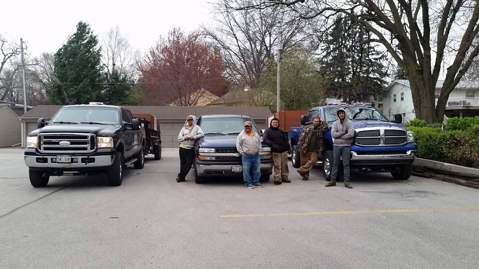 A group of men are standing in front of trucks in a parking lot