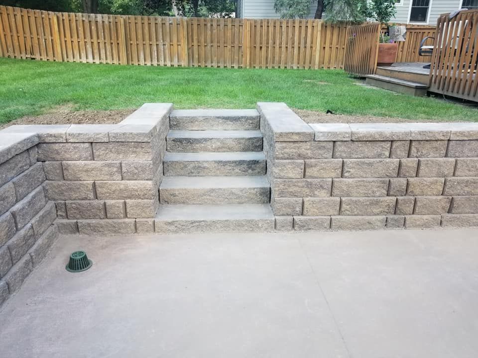 A brick wall with stairs leading up to a patio and a wooden fence in the background.