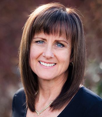 A woman in a grey jacket and red shirt smiles for the camera