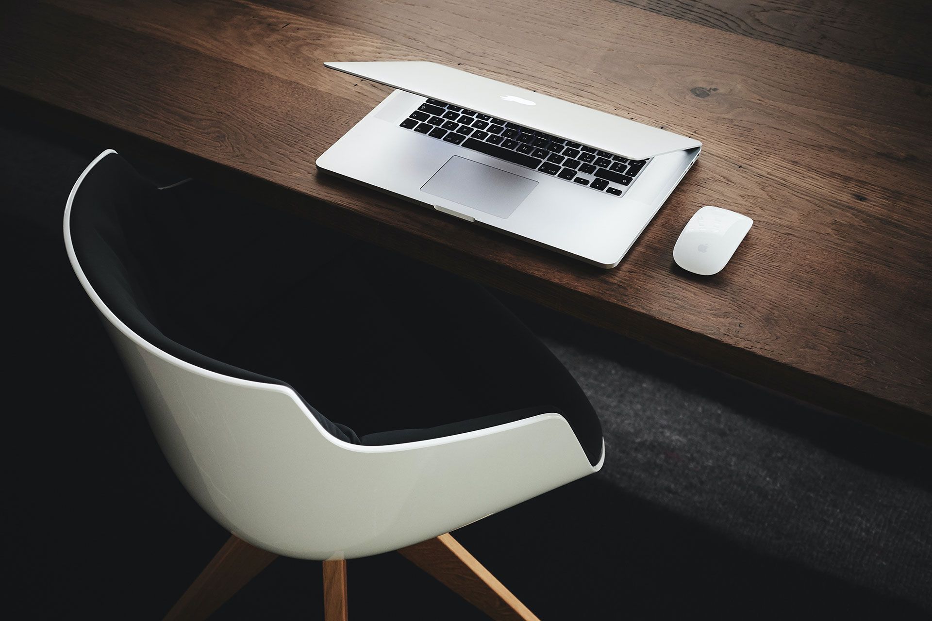 A laptop computer is sitting on a wooden desk next to a chair.