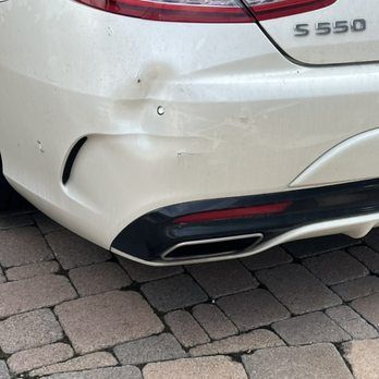 A white Mercedes-Benz S550 with a dented rear bumper parked on a paver driveway.