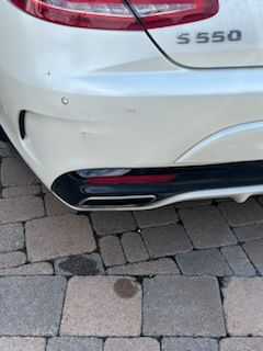 Close-up view of the rear bumper of a white Mercedes-Benz S 550 parked on a paved driveway.
