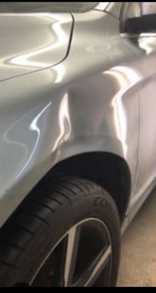 A silver car fender with a dent visible above the front wheel arch.