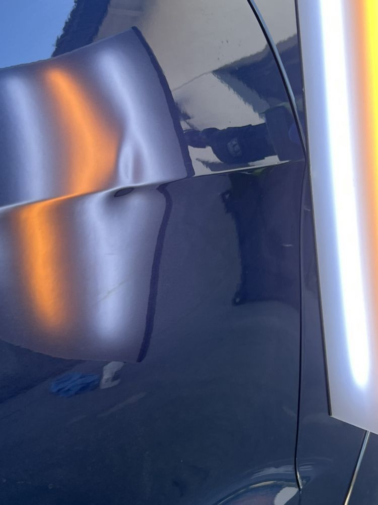 A dent on a dark vehicle door panel reflecting light from a PDR inspection lamp.