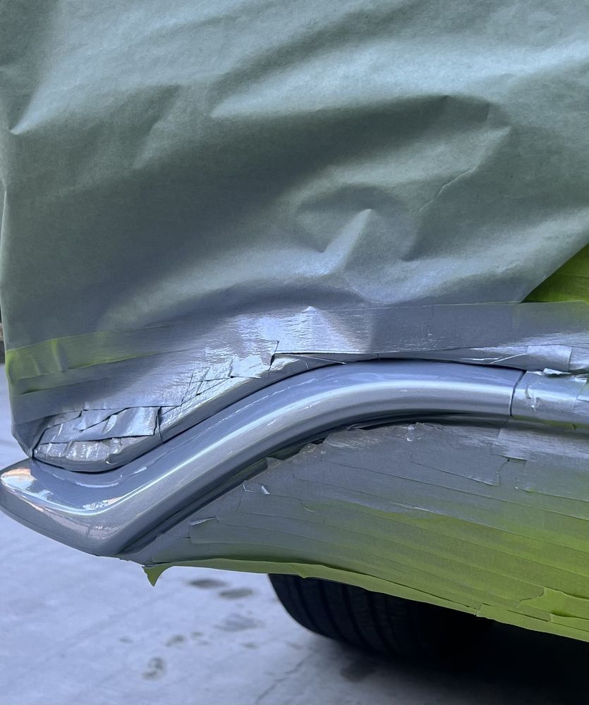 A damaged vehicle bumper covered in protective tape, showing peeling paint and structural deformation during repairs.