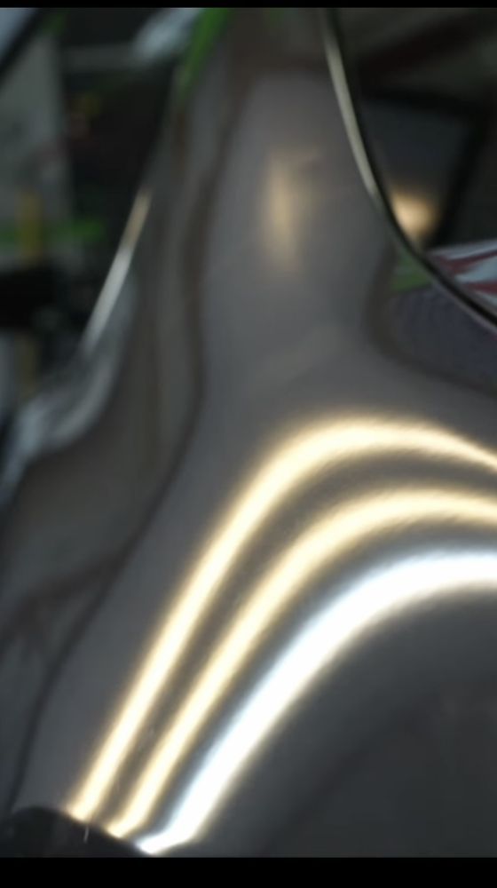 Reflections of bright, curved light lines on a smooth, dark automotive body panel.
