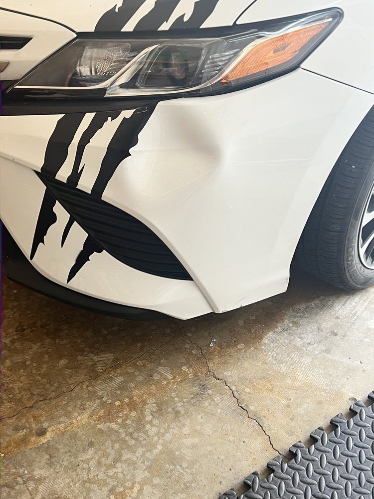 A white car bumper with a dent below the headlight and black claw-mark decals.