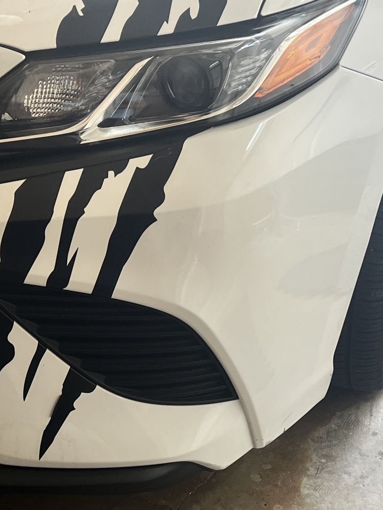 A close-up of the front driver-side headlight and bumper of a white car with black claw mark decals.